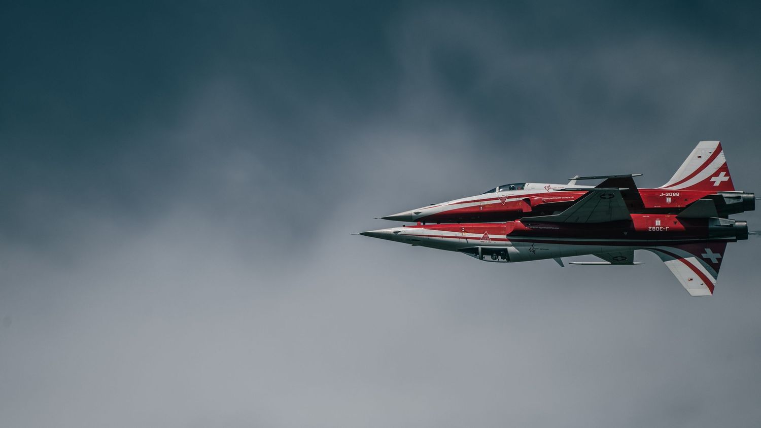 Red and black military jet fighter performing aerobatic maneuver against overcast grey sky.