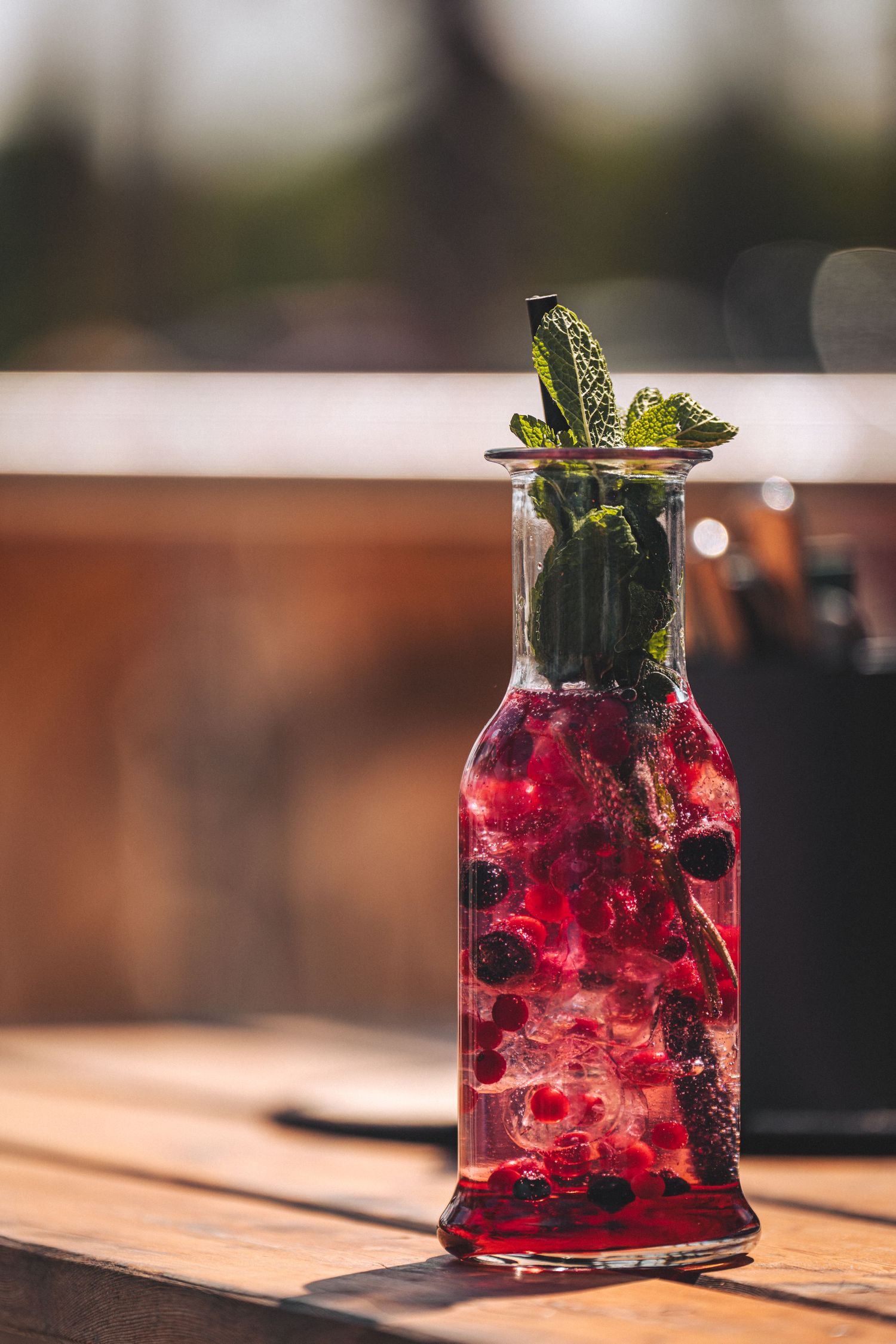 Berry lemonade cocktail in a glass bottle garnished with fresh mint on a wooden table.