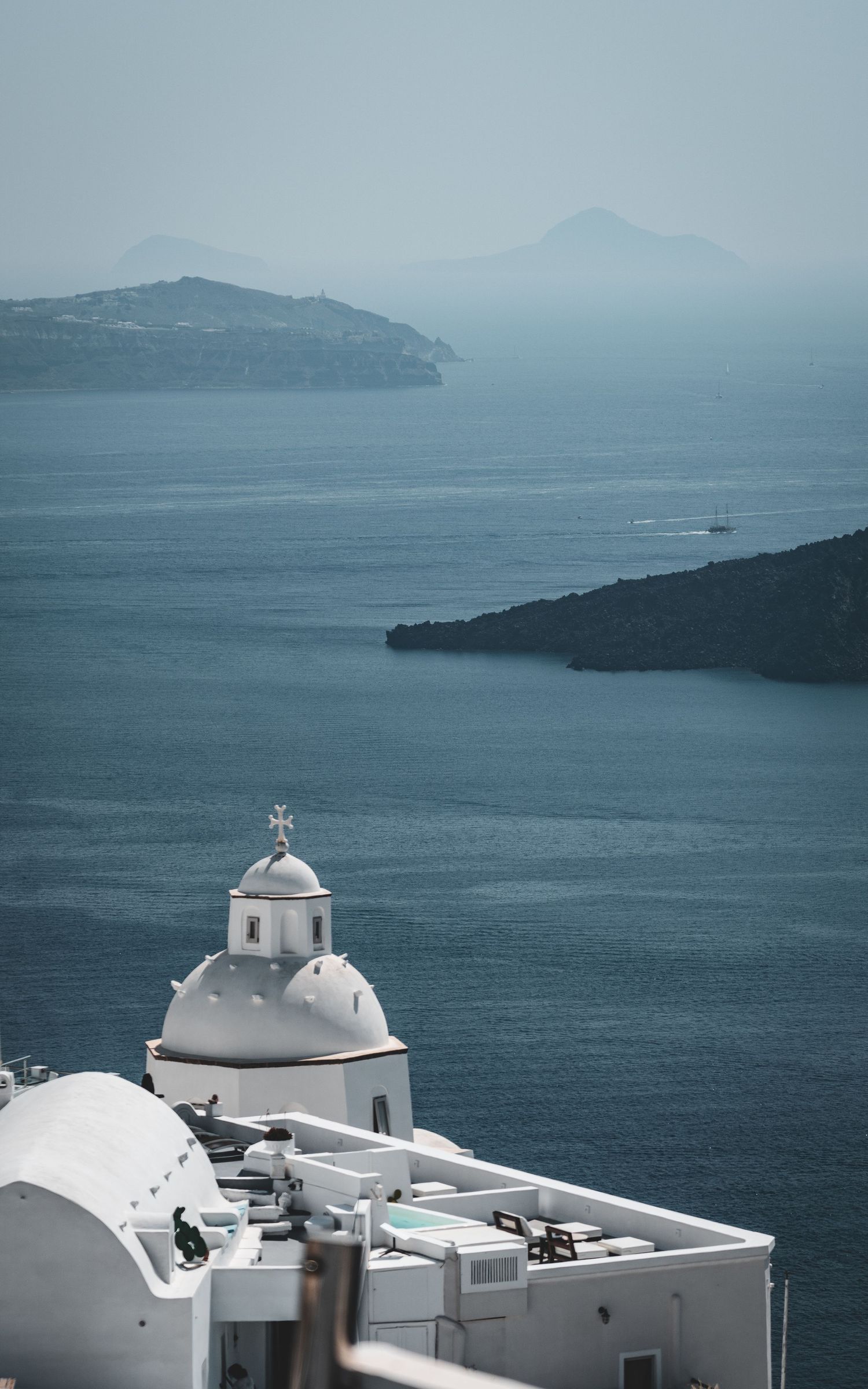 White domed Greek Orthodox church overlooking the deep blue caldera sea in Santorini, Greece.