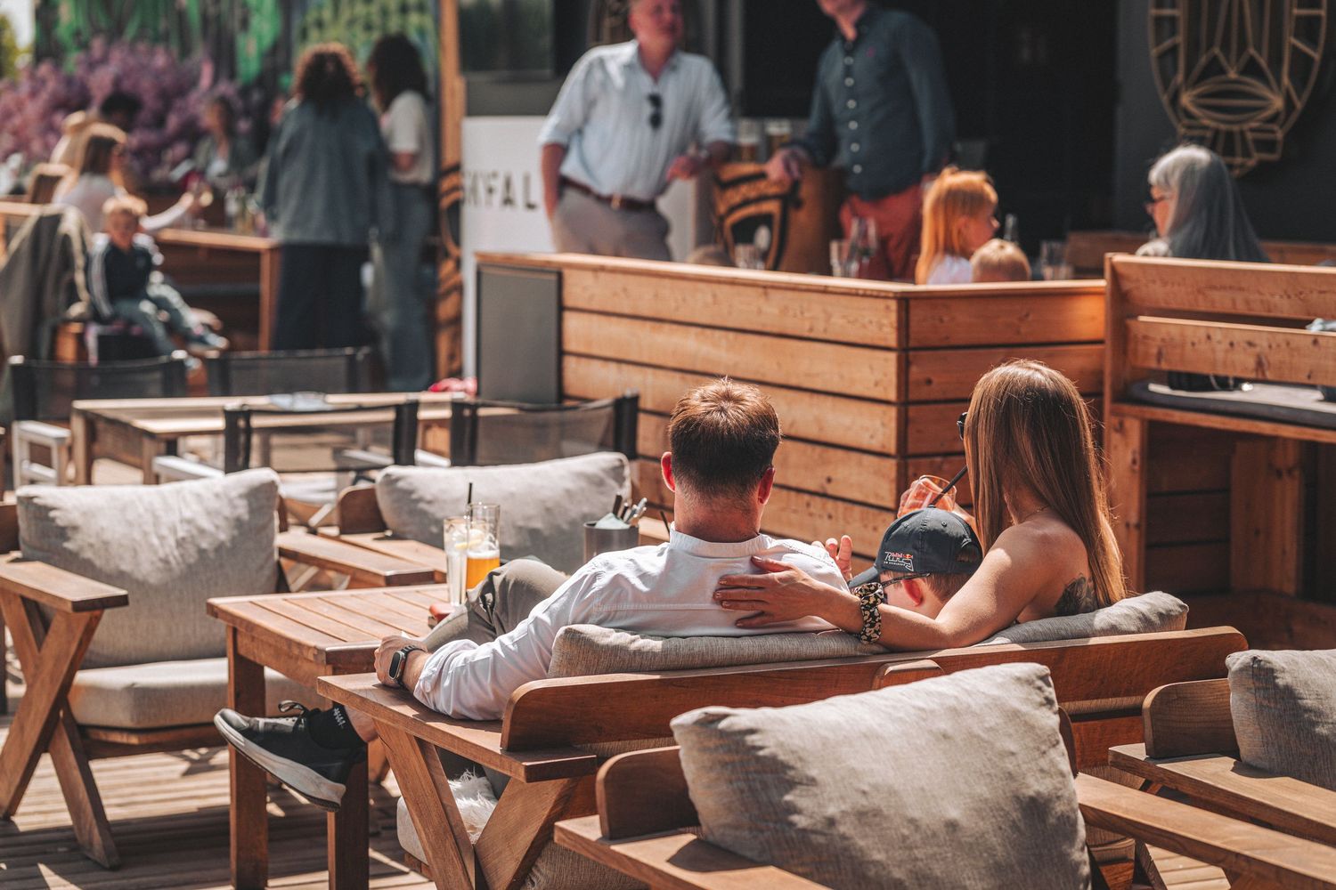 Couple relaxing together at a sunny outdoor restaurant patio with wooden furniture.