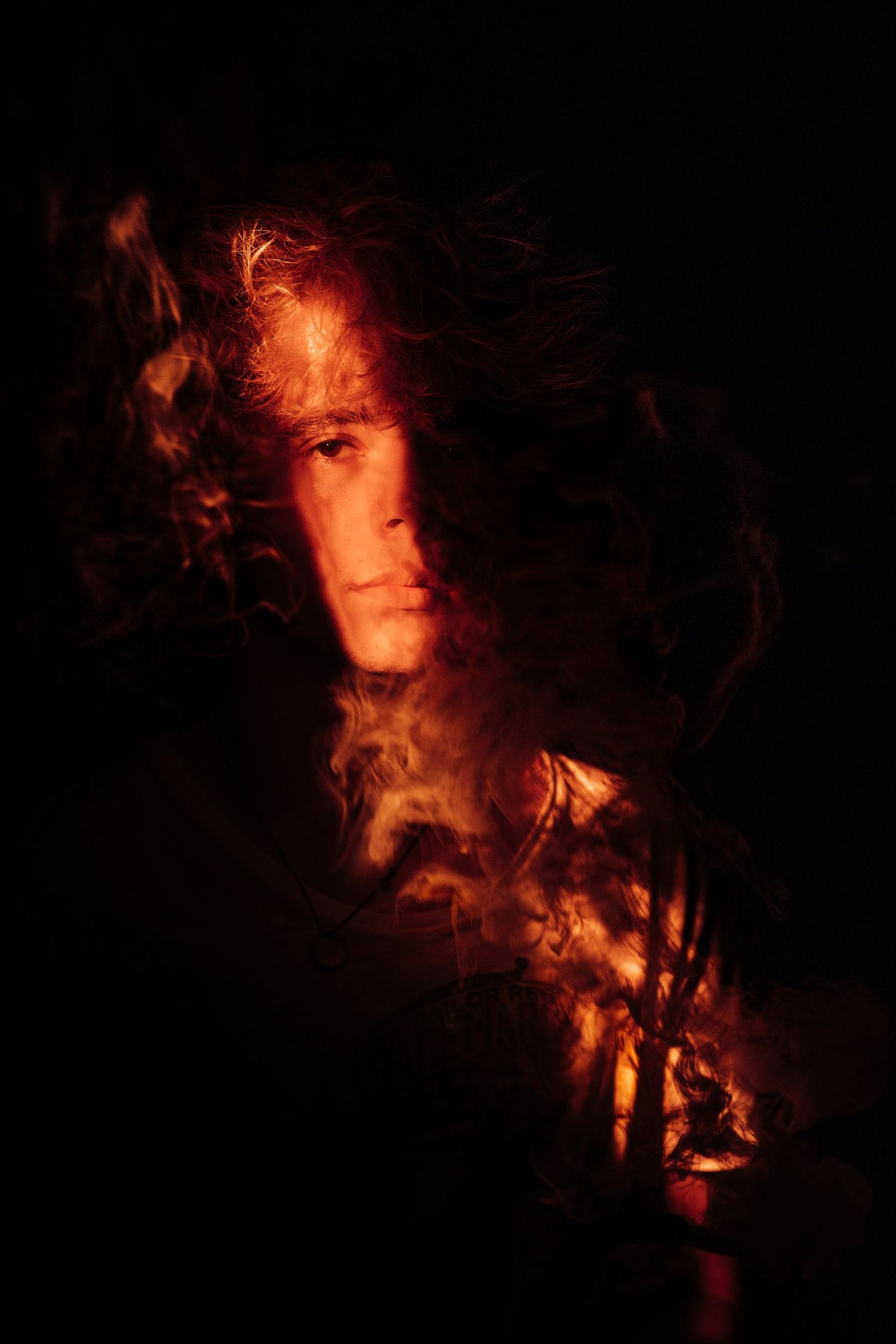 Dramatic portrait of a person surrounded by glowing red and orange smoke against a dark background.