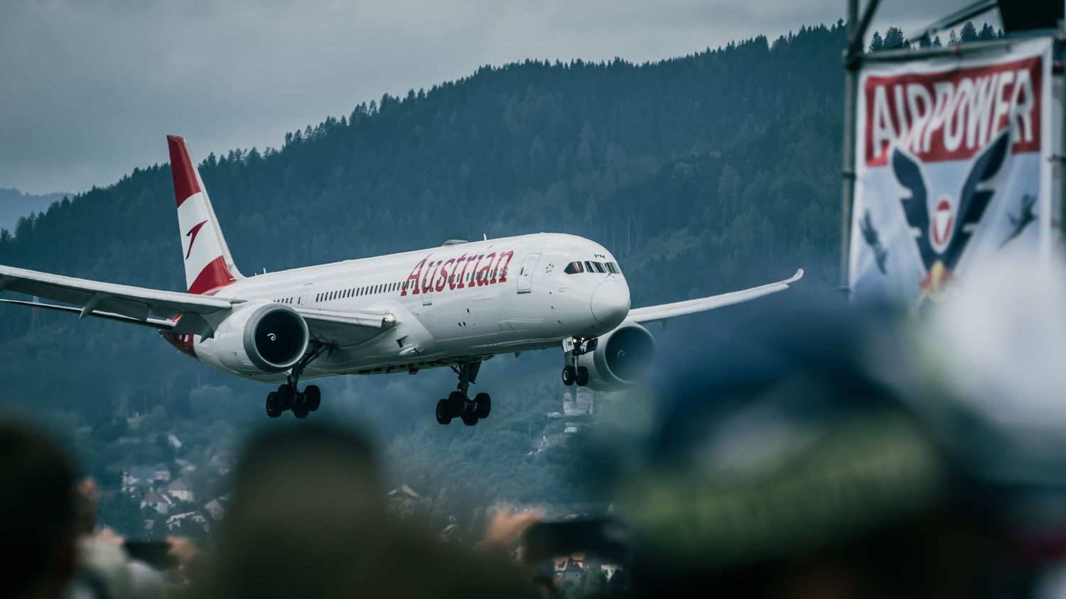 Austrian Airlines commercial aircraft on approach to land at airshow with mountain backdrop.