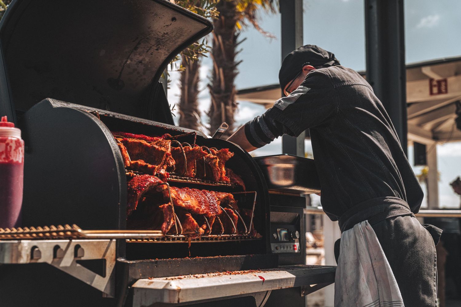 Chef tending to smoked BBQ ribs on a large outdoor smoker grill.