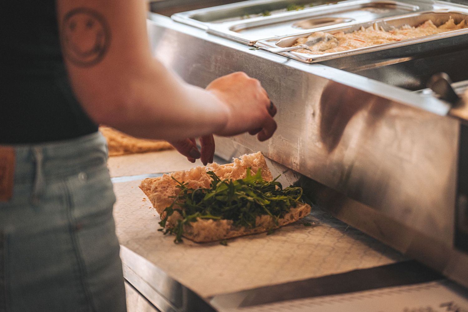 Chef preparing a fresh herb-topped flatbread or pizza at an outdoor food service station.