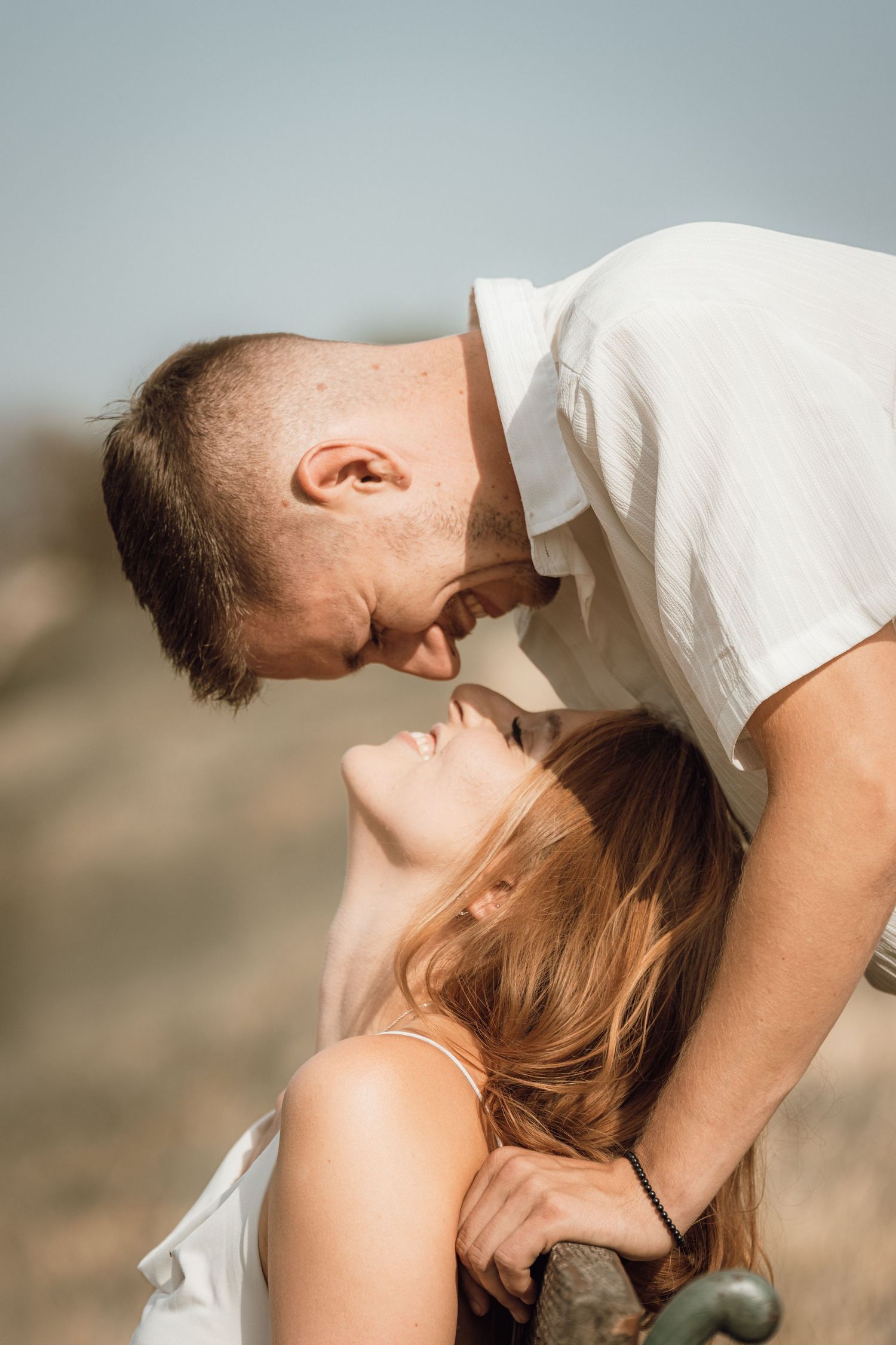 Romantic couple sharing an intimate moment outdoors, man leaning in to kiss woman in natural sunlit setting.