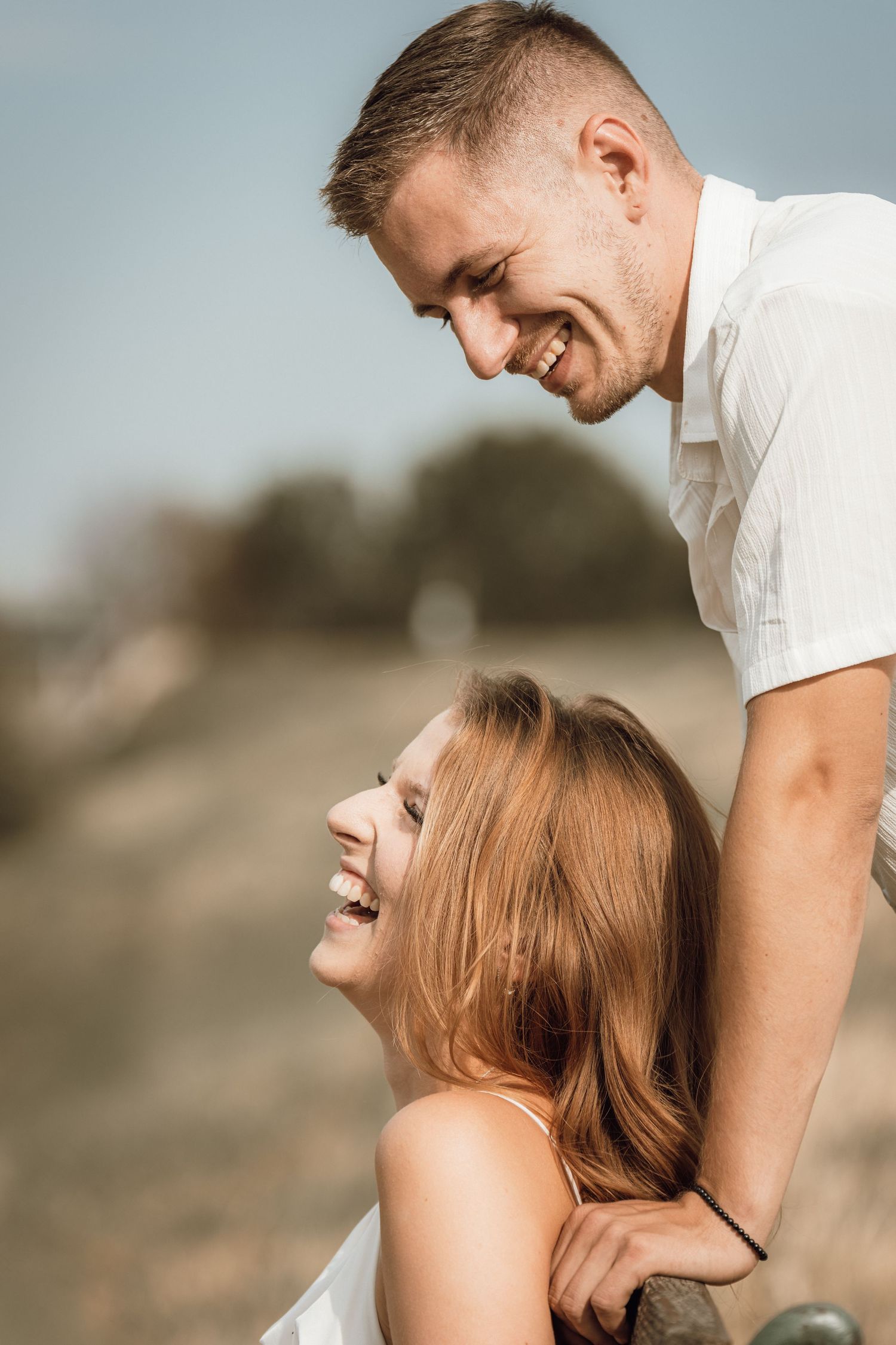 A happy young couple laughing and sharing a joyful moment outdoors on a sunny day in a field.