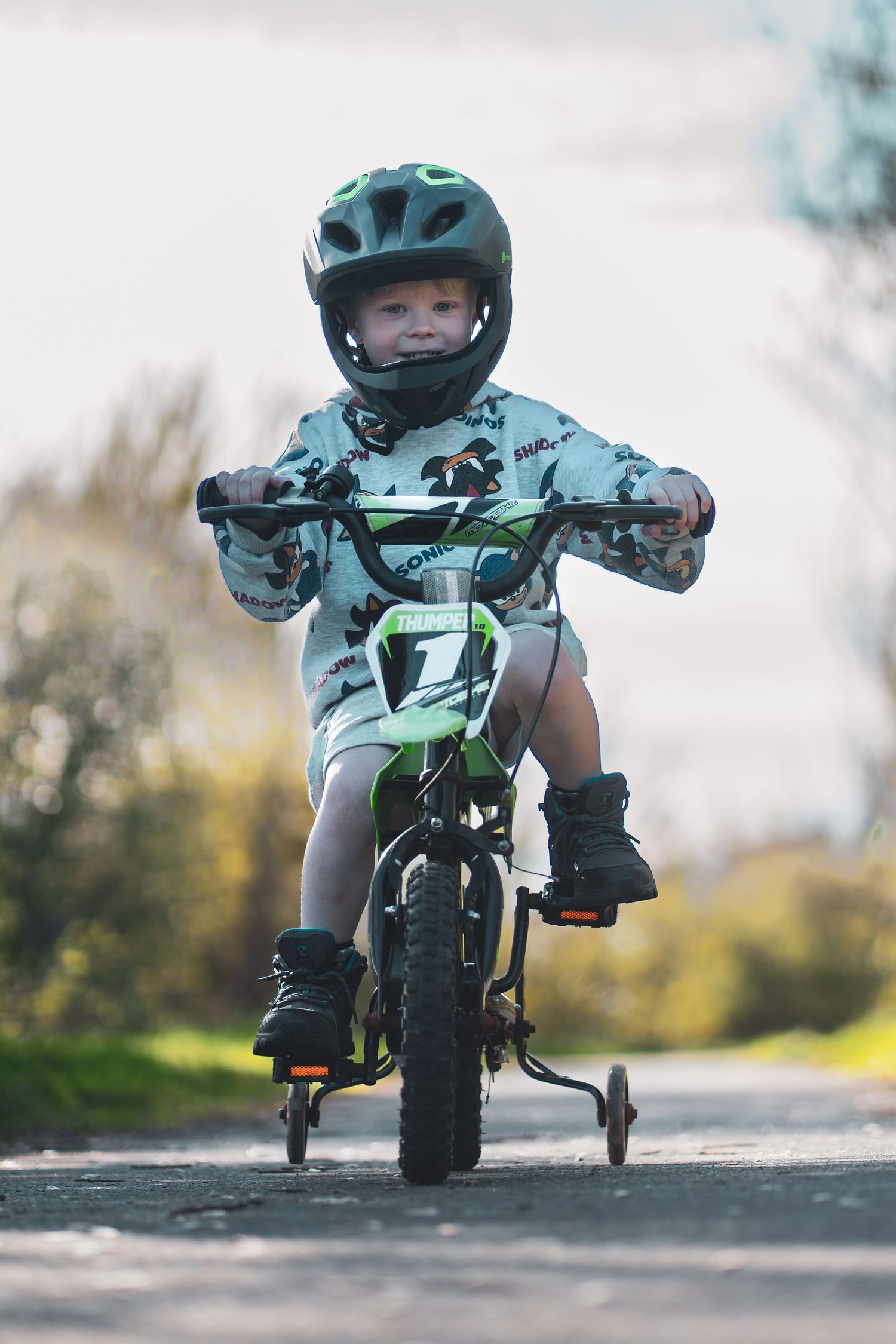 A child wearing a helmet riding a bicycle towards the camera on a paved path.