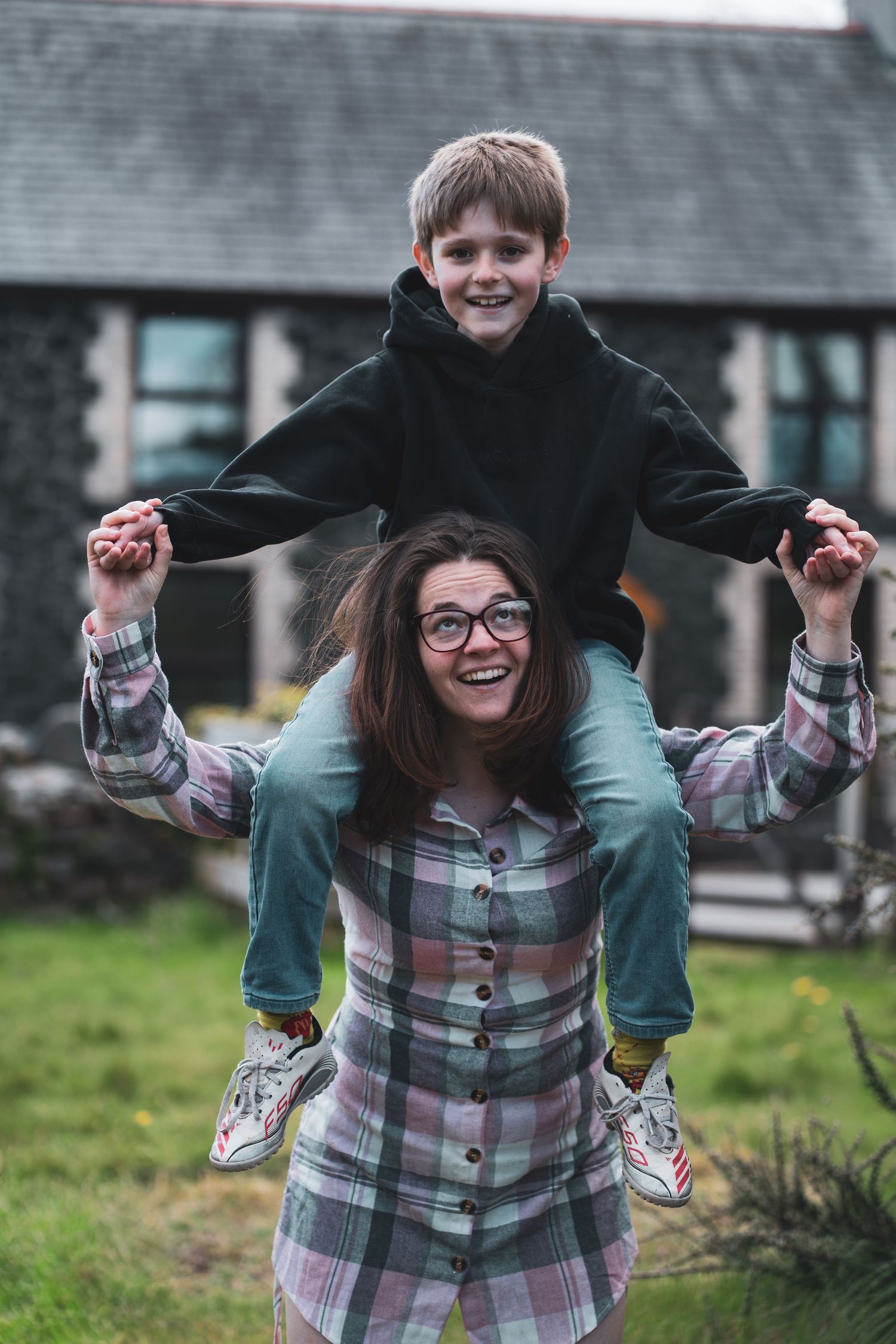 A smiling adult carrying a child on their shoulders in a garden.