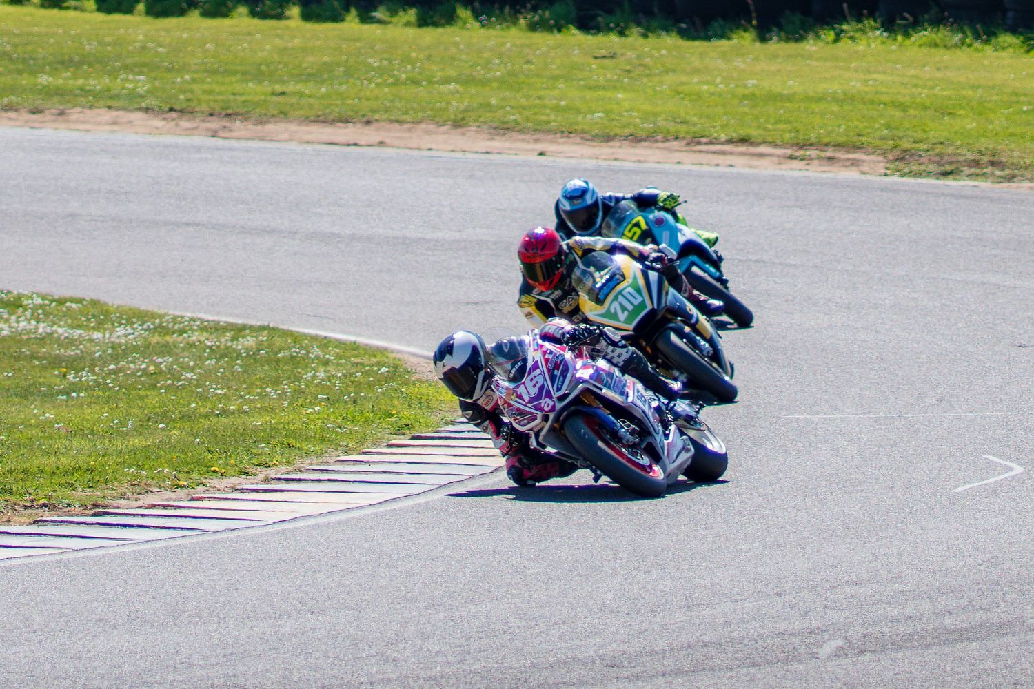 A group of motorcycle racers leaning into a bend on a racetrack.
