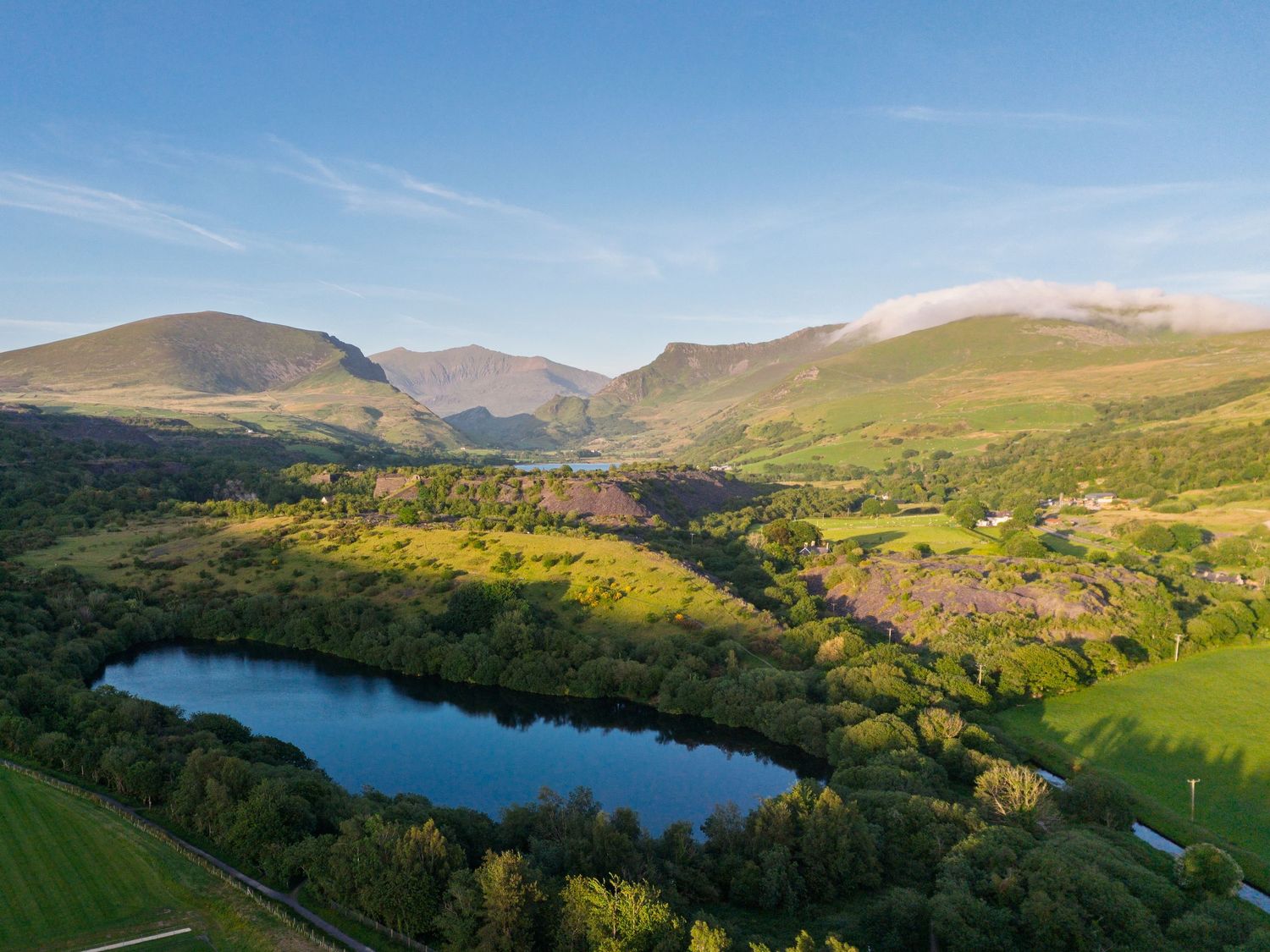 Aerial view of a small lake nestled in a lush green valley with mountains.