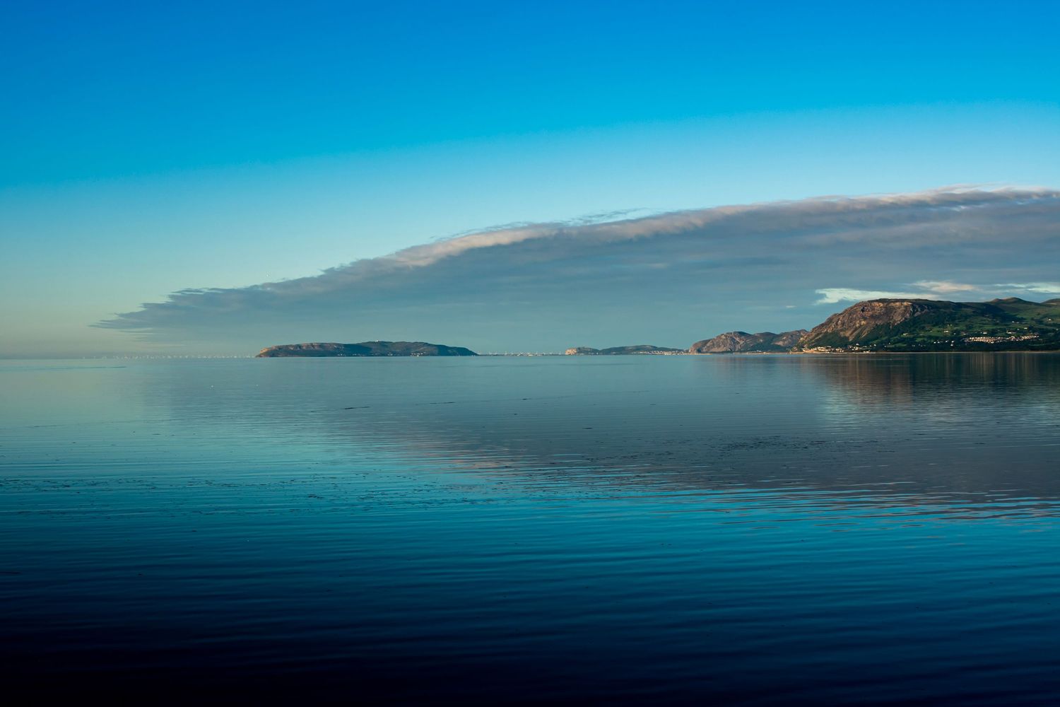 Calm blue ocean waters reflecting a cloudy sky with distant islands on the horizon.