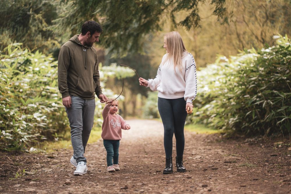 Two adults walking hand in hand with a young child along a woodland path.