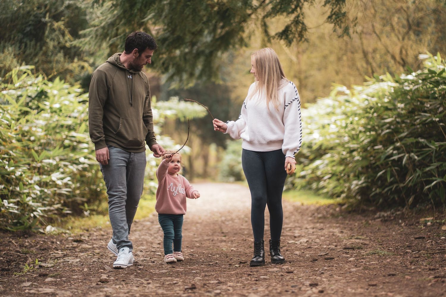 Two adults walking hand in hand with a young child along a woodland path.