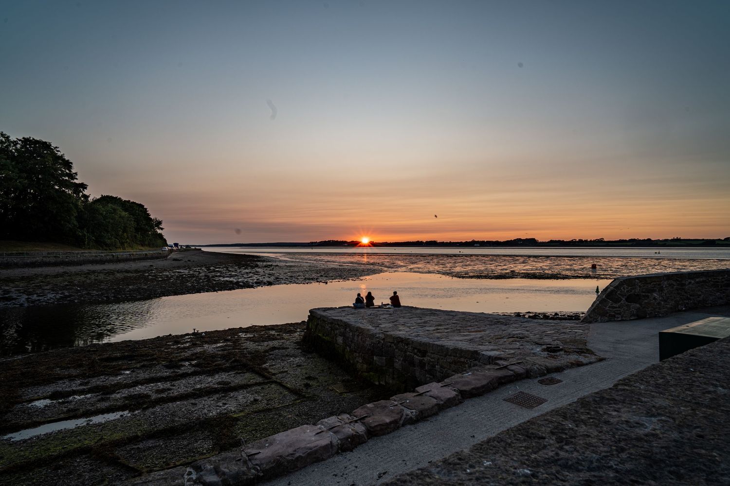 Sunset over a quiet shoreline, with stone slipways leading towards the water.