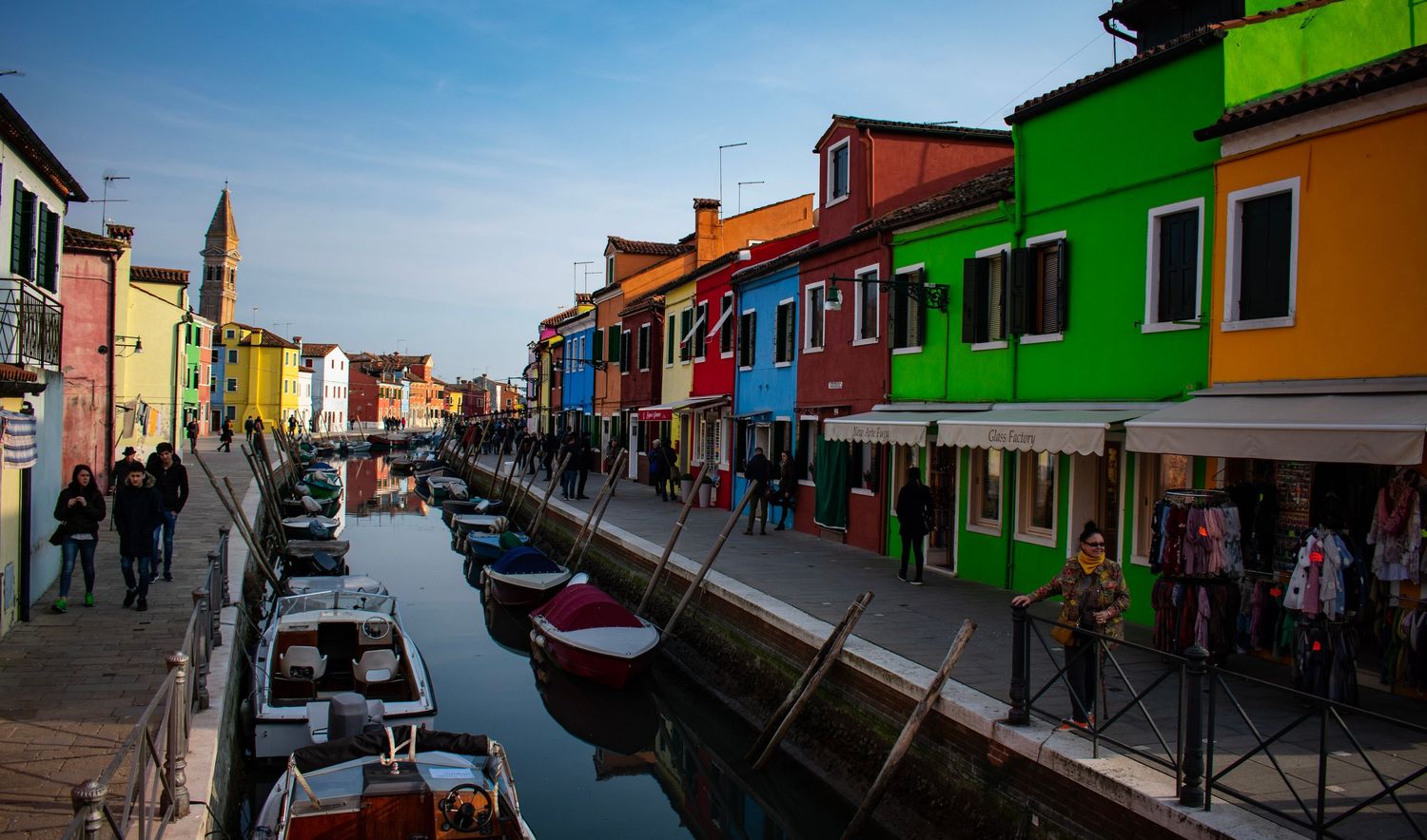 Colorful buildings lining a canal in Burano Italy with boats and tourists along the waterfront.