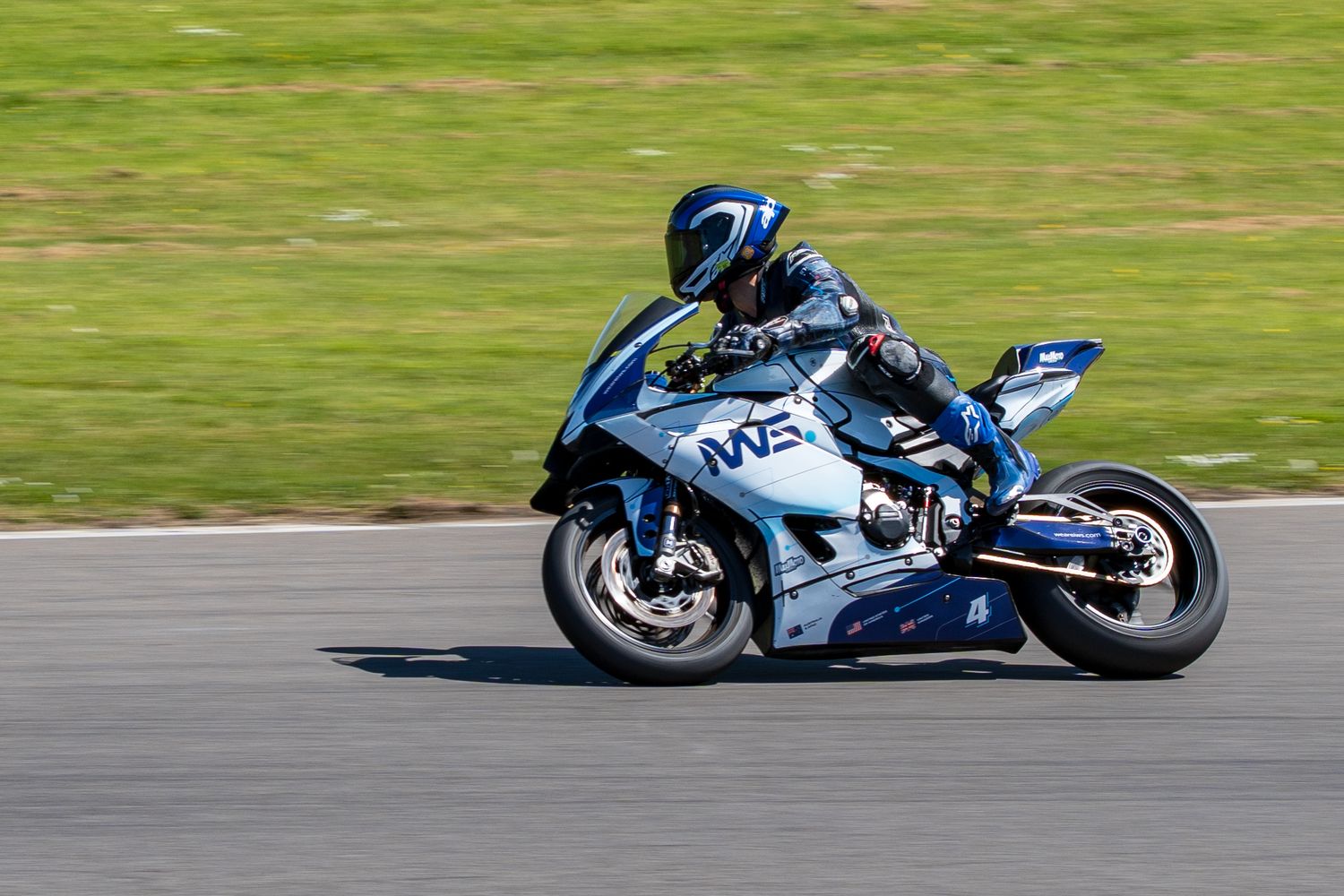 Blue racing motorcycle with rider in full gear leaning into a turn on a race track.