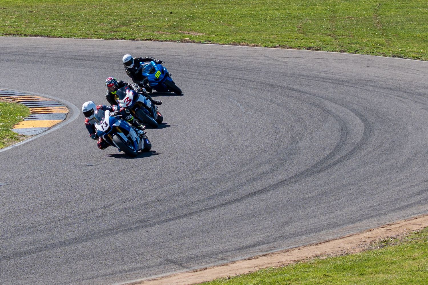 Three motorcycle racers leaning through a sweeping bend on a racetrack.