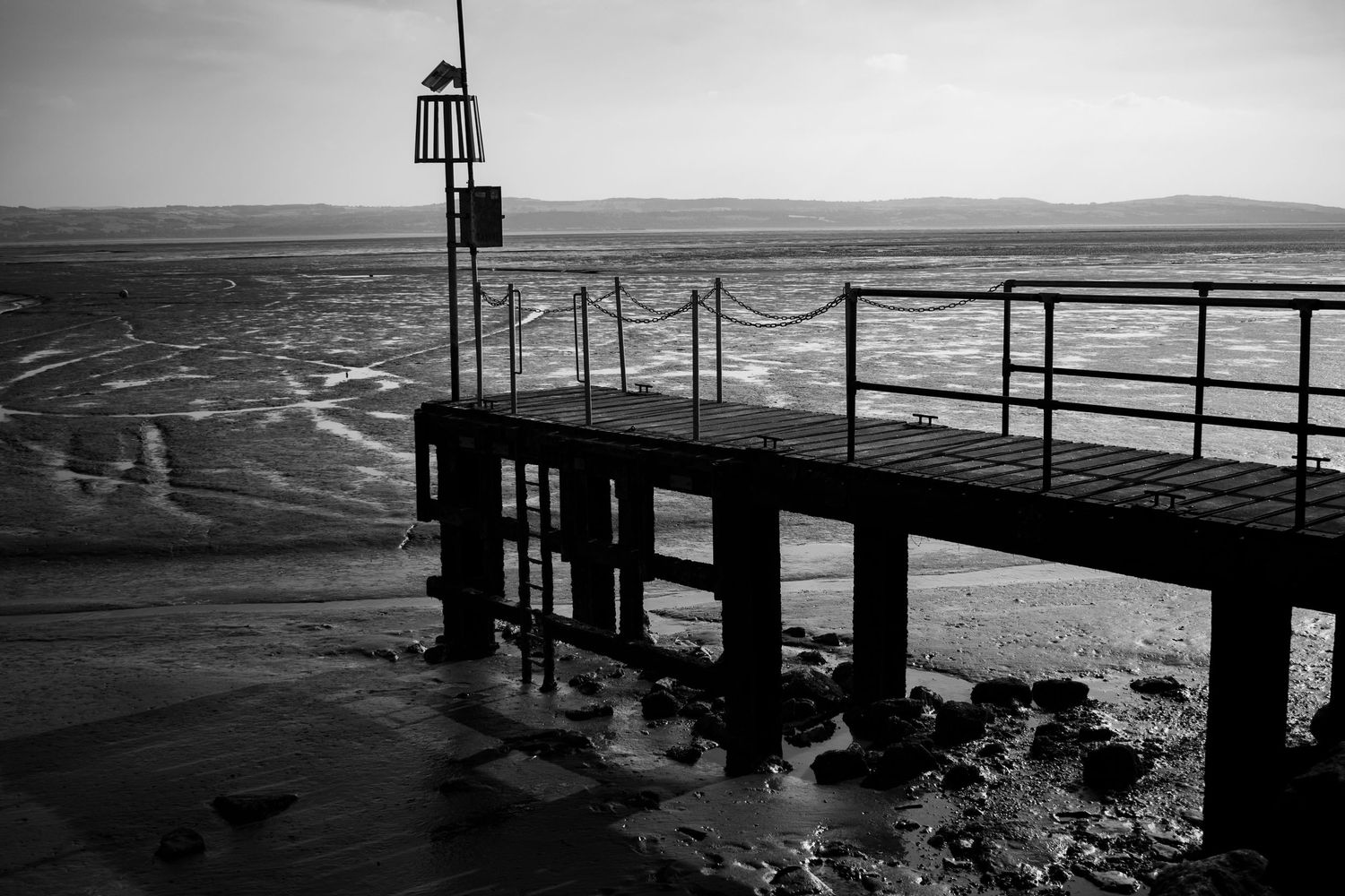 Black and white photograph of a small jetty with metal railings extending over the water.