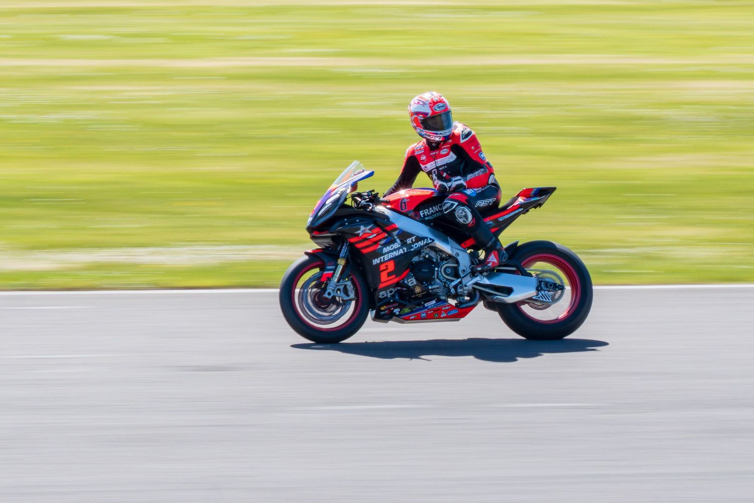 Red and black racing motorcycle with rider in matching gear on a sunny race track.