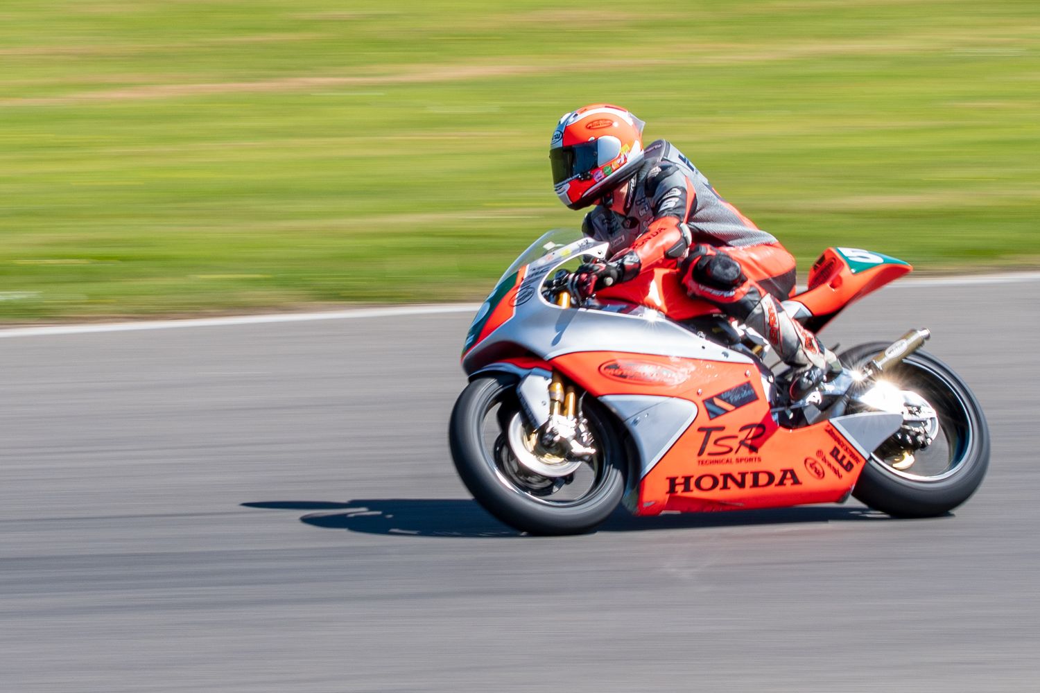 Rider on an orange and white Honda racing motorcycle speeding along a racetrack.