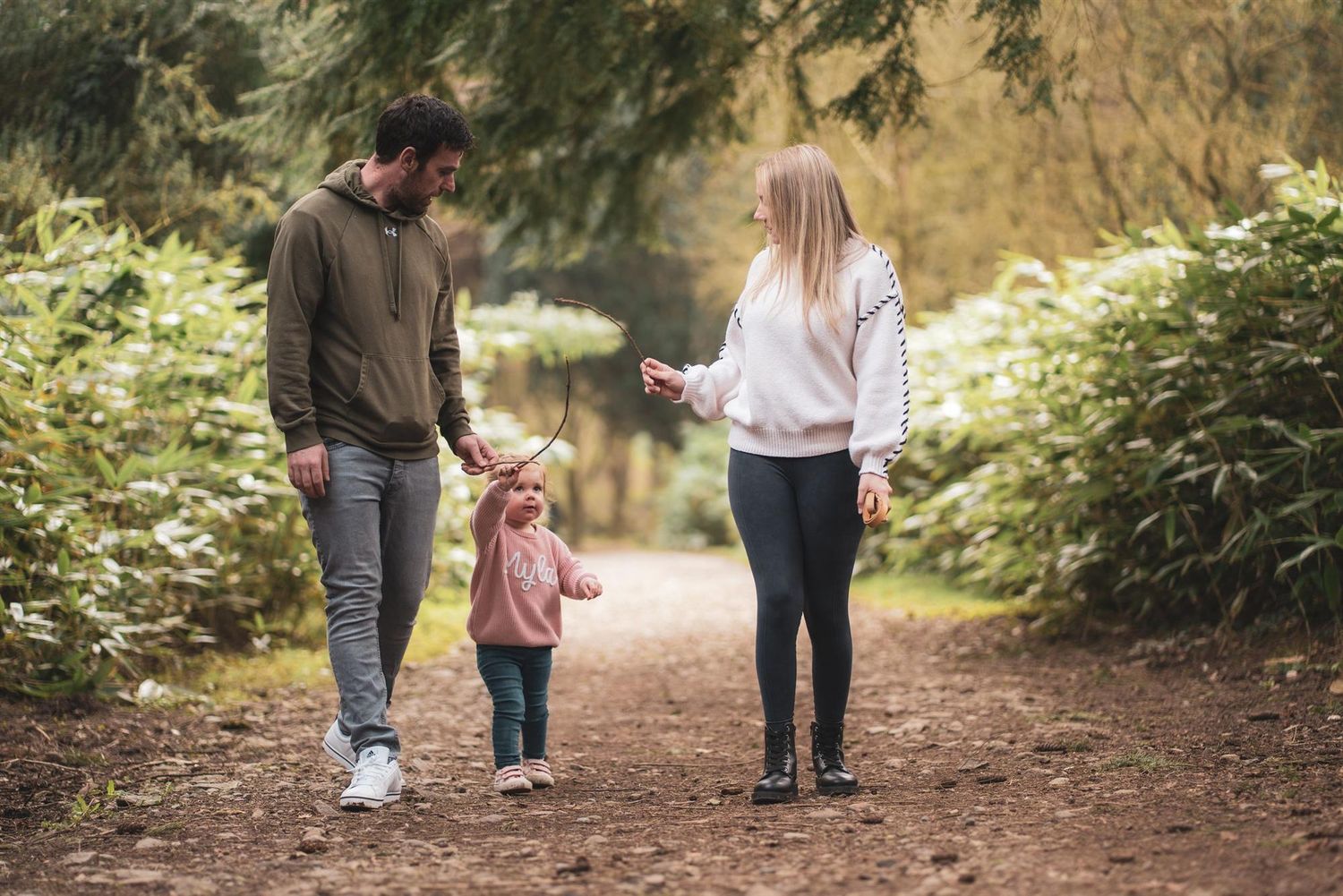 Two adults walking hand in hand with a young child along a woodland path.