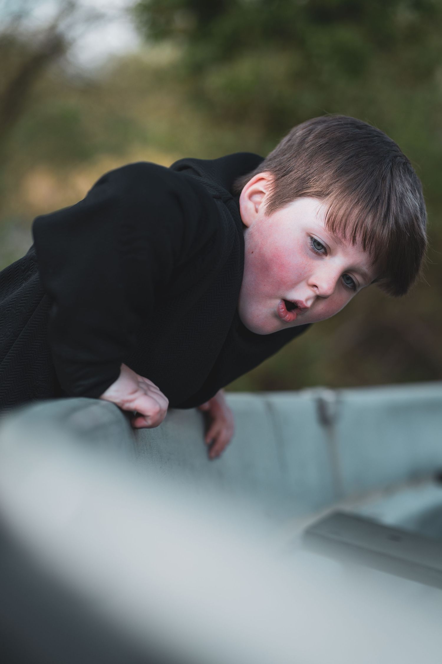 A child leaning over a pale railing outdoors and looking towards the camera.