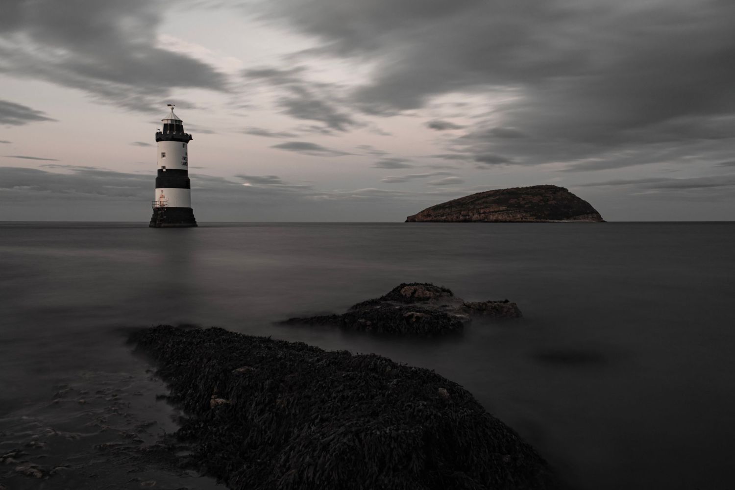 Black and white long exposure photo of Penmon Lighthouse with Puffin Island at dusk in Wales.