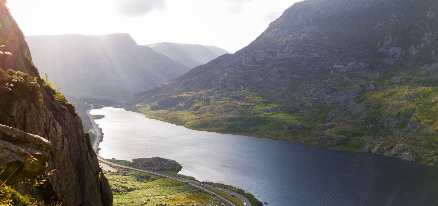 Sunlight streams between steep mountains above a lake in a green, rocky valley.