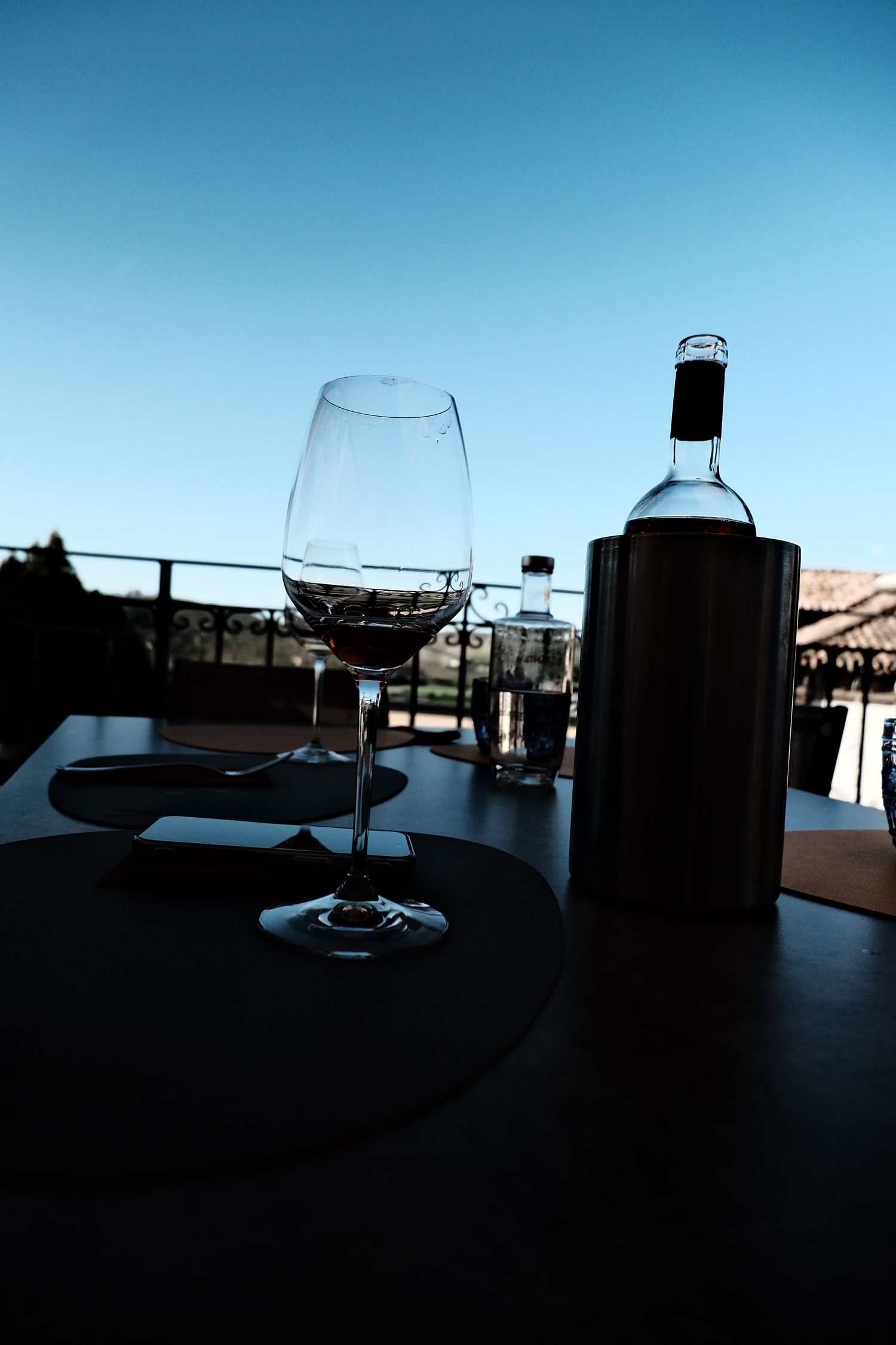 Glass of wine and a bottle in a cooler on a terrace table against a deep blue sky in Italy