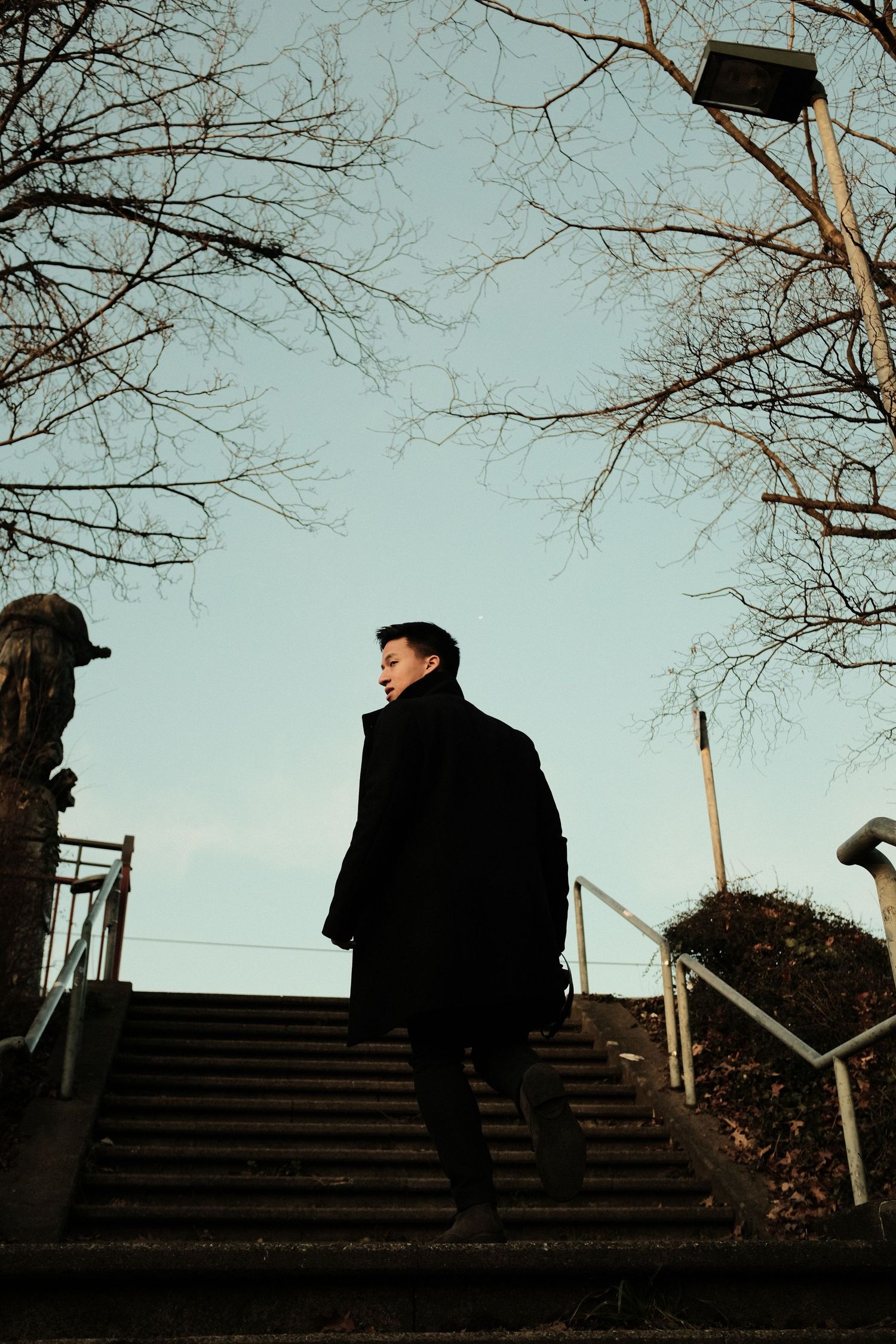 Man in a dark coat climbing stone stairs under bare winter trees in Düsseldorf