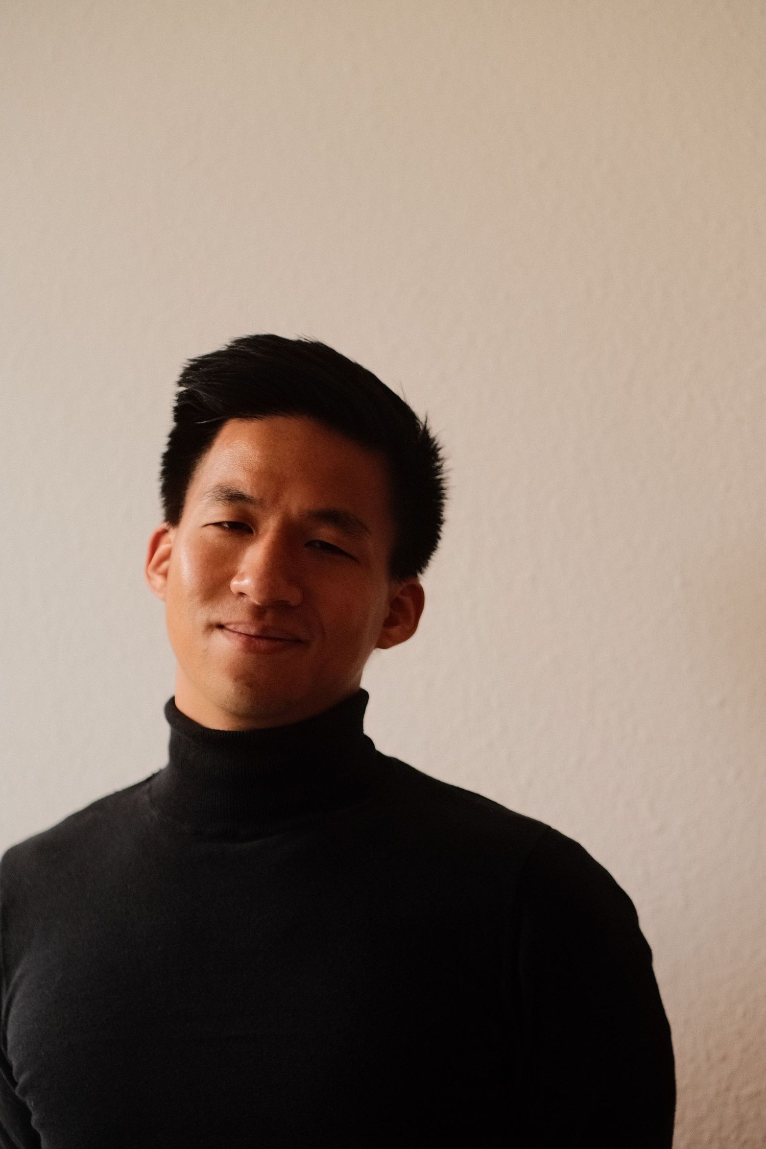 Portrait of Düsseldorf travel photographer Dinh Huy in a black turtleneck against a warm beige wall