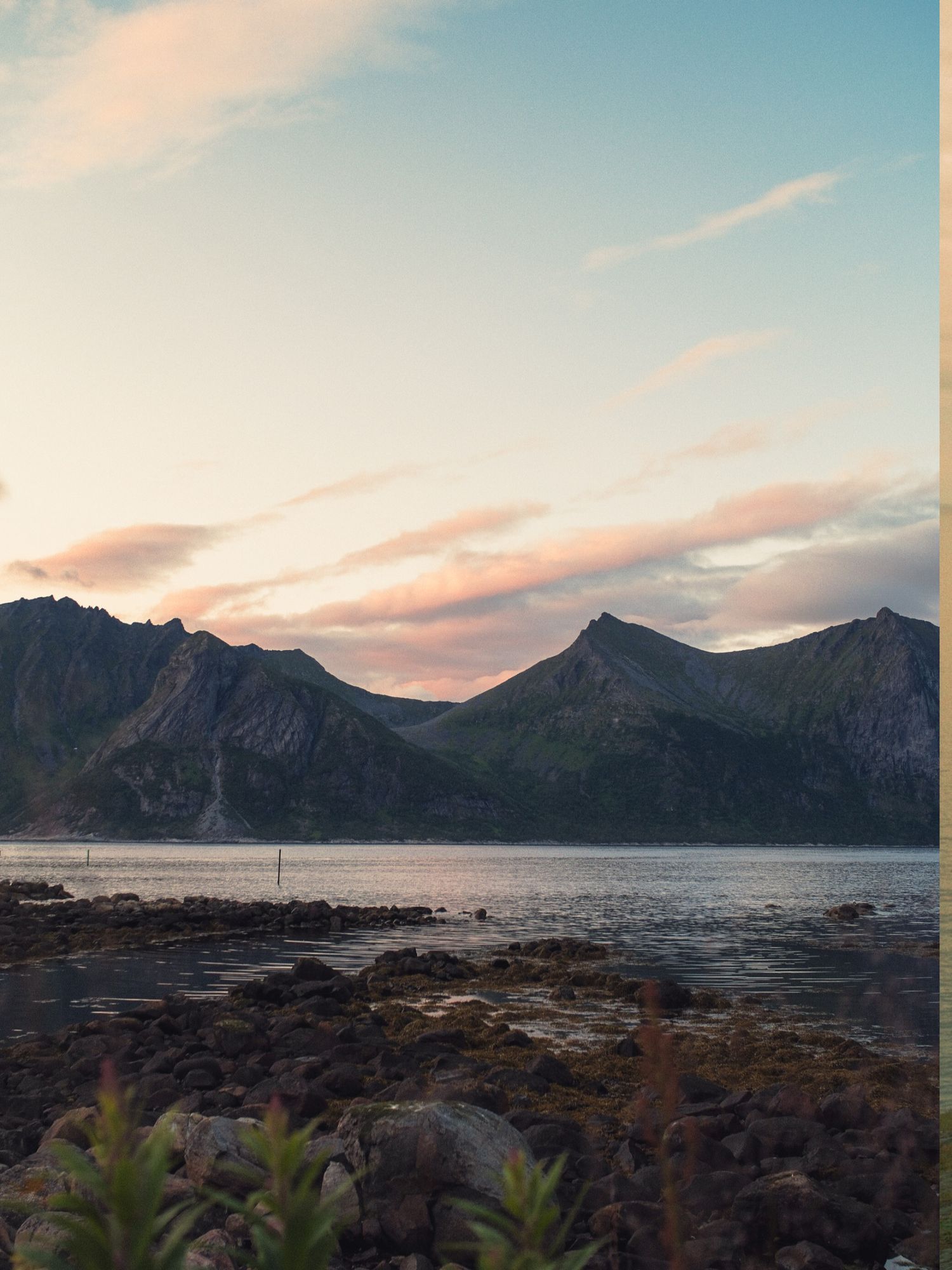 Rocky shoreline and snow-dusted mountains at golden hour on Senja, Norway