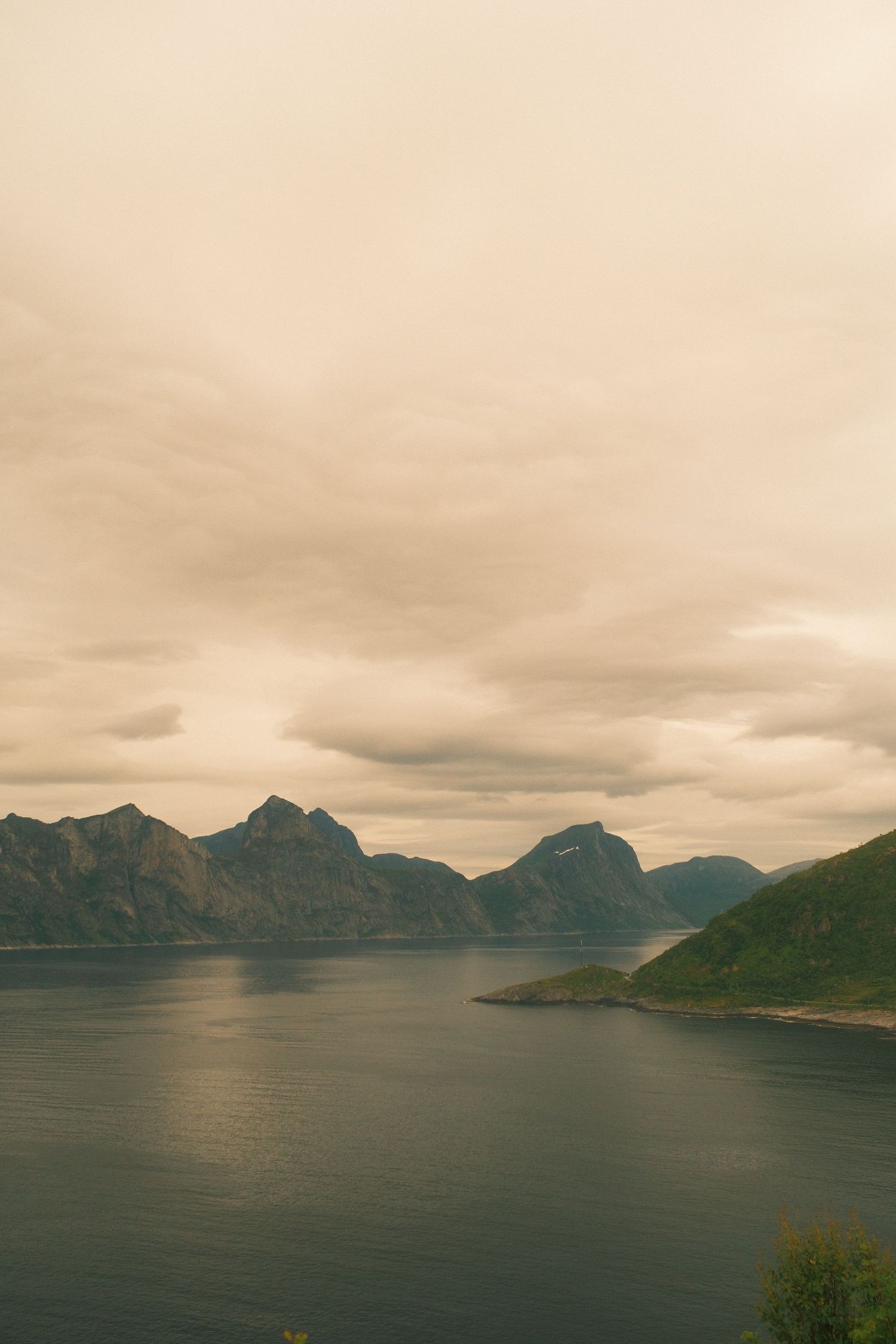 Soft evening light over jagged peaks and a still fjord on Senja, Norway