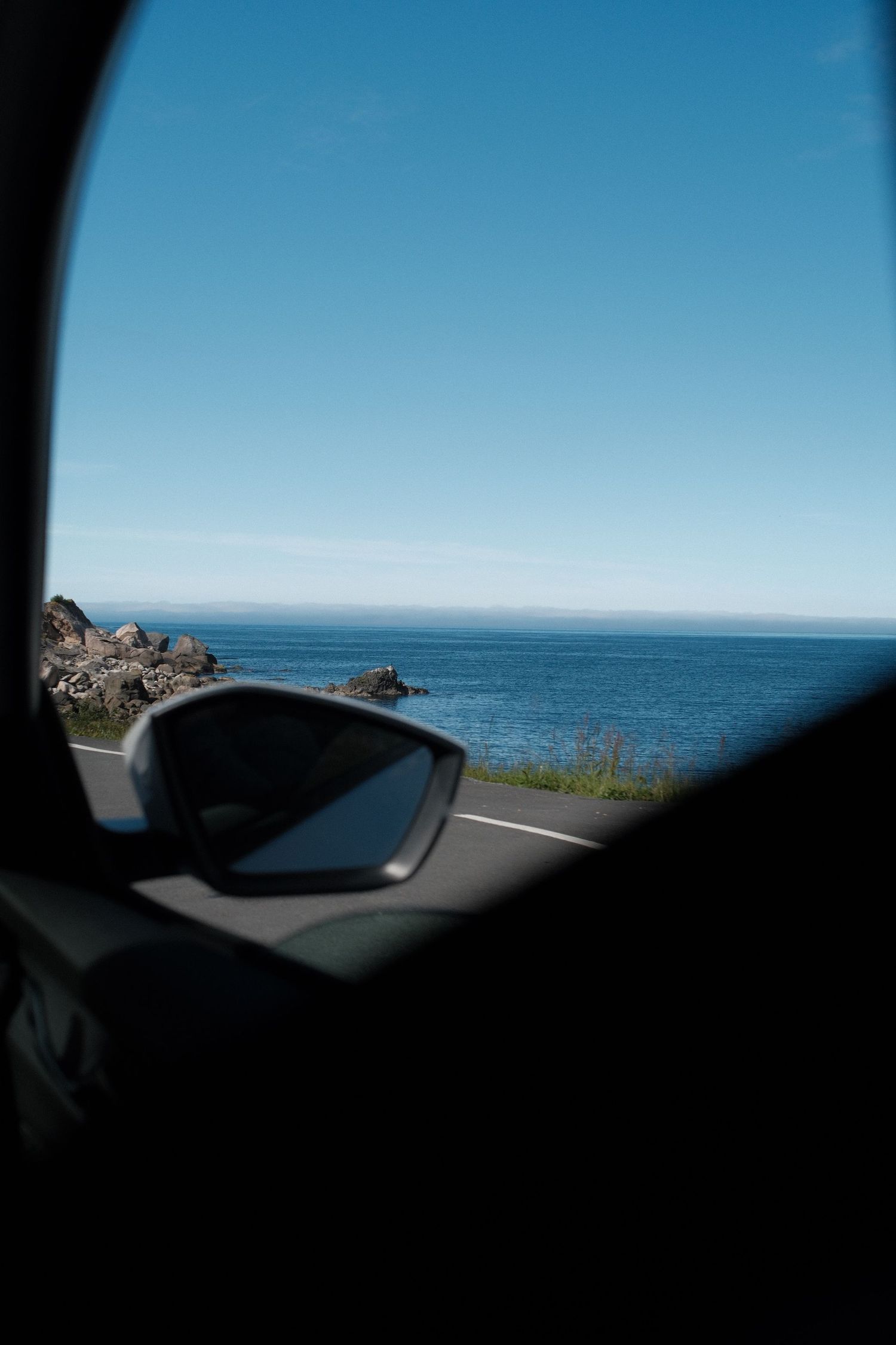 Blue sea seen through a car window and side mirror on a Norwegian road trip