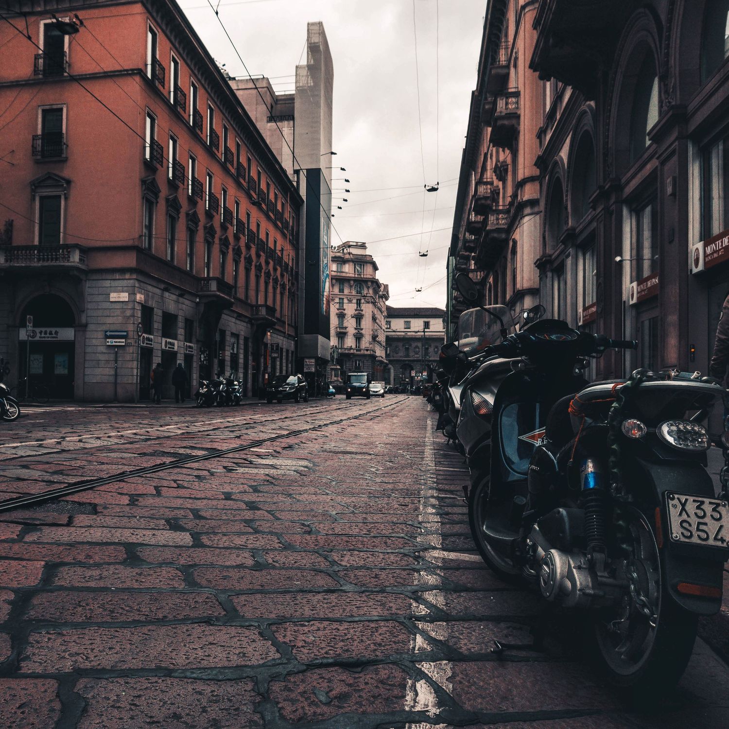 Cobbled street in an old Italian town with scooters parked along the kerb under a grey sky