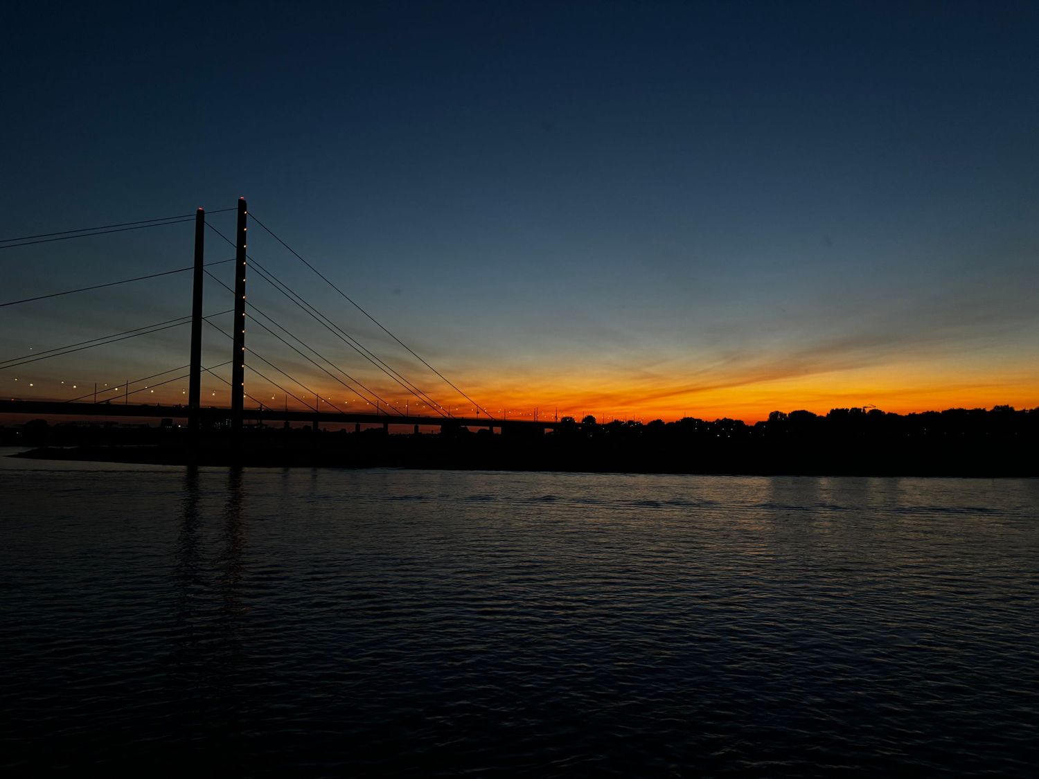 Cable-stayed Rhine bridge silhouetted against an orange sunset over the river in Düsseldorf