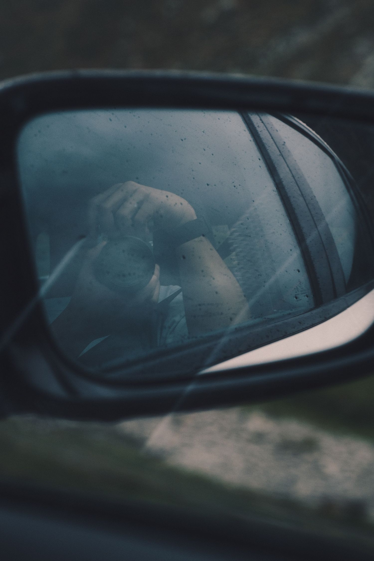 Photographer with a camera reflected in a car wing mirror on a rainy drive over the Gotthard Pass