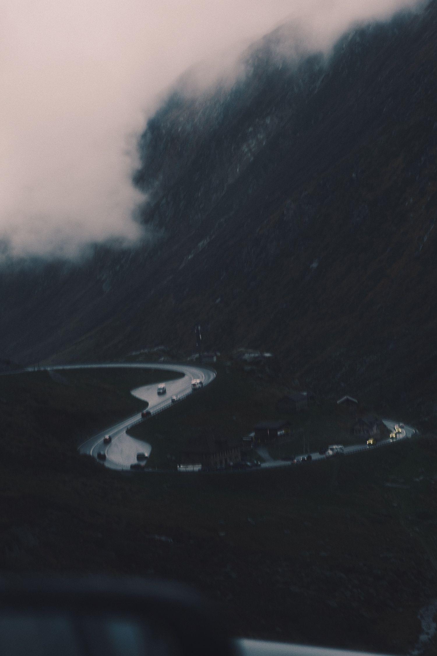 Pale pink sky over a dark forested valley and winding road near the Gotthard Pass