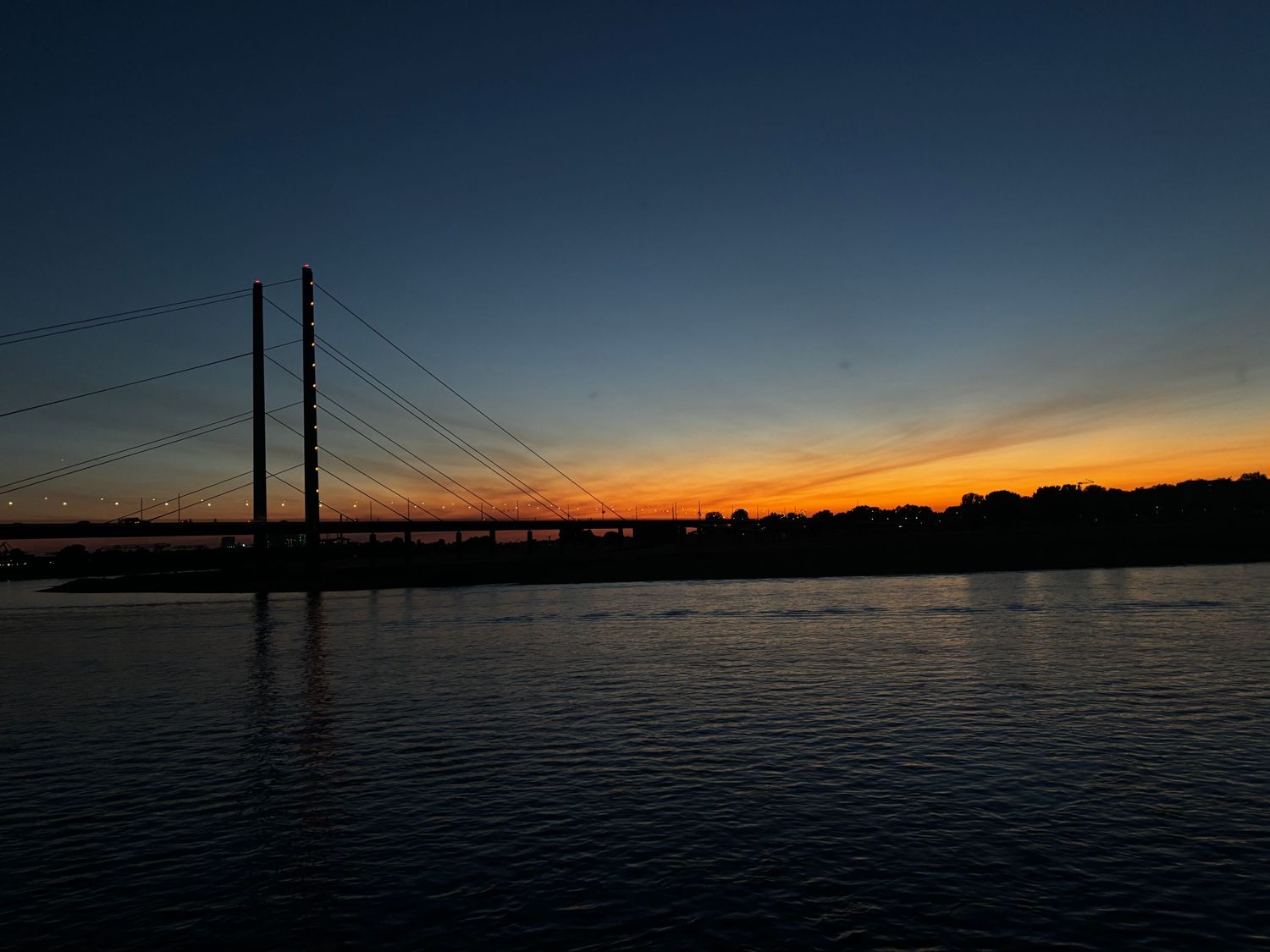 Cable-stayed Rhine bridge in Düsseldorf against an orange sunset sky