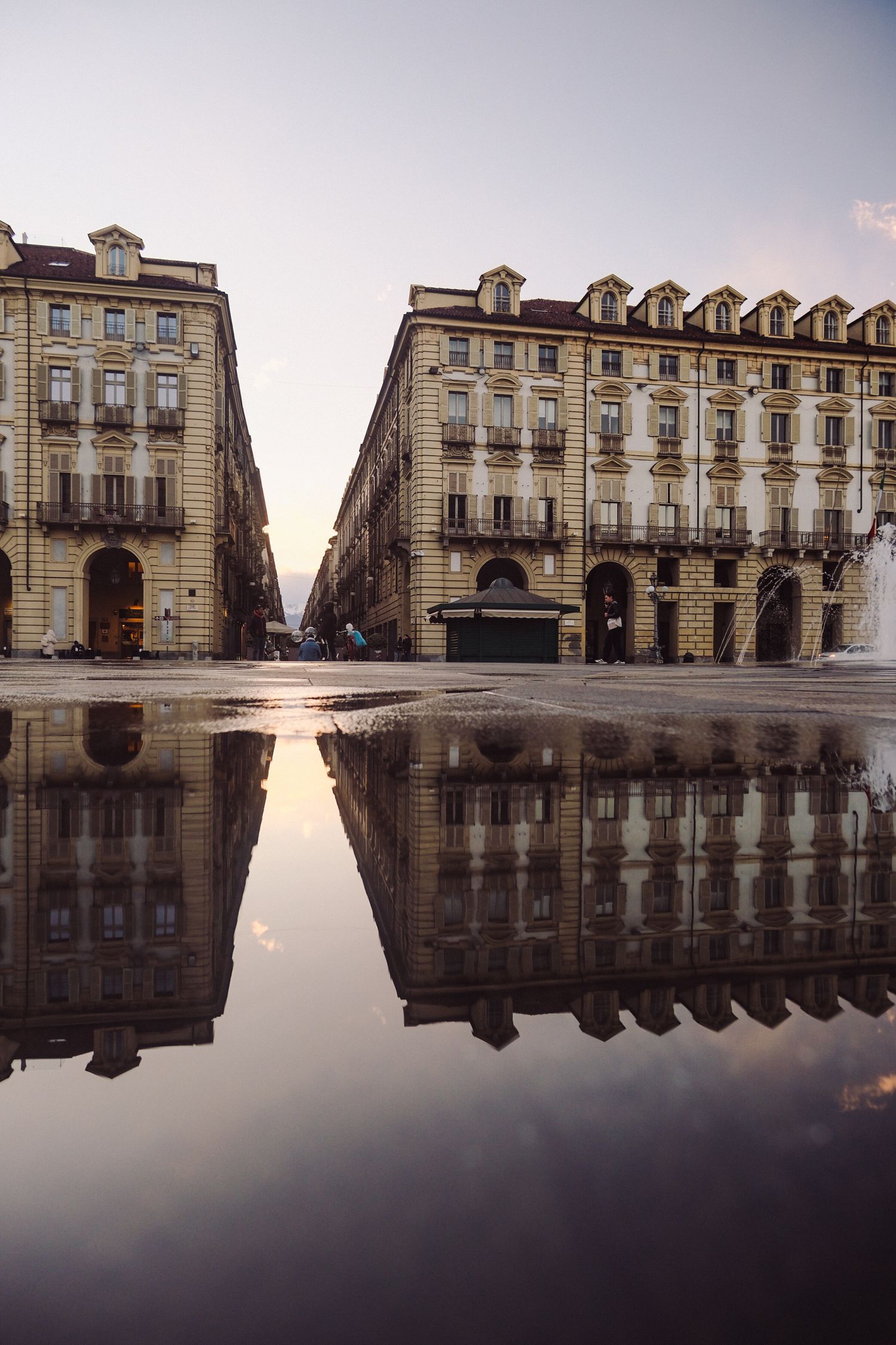 Arcaded buildings on an empty piazza in Turin mirrored in a rain puddle at dawn