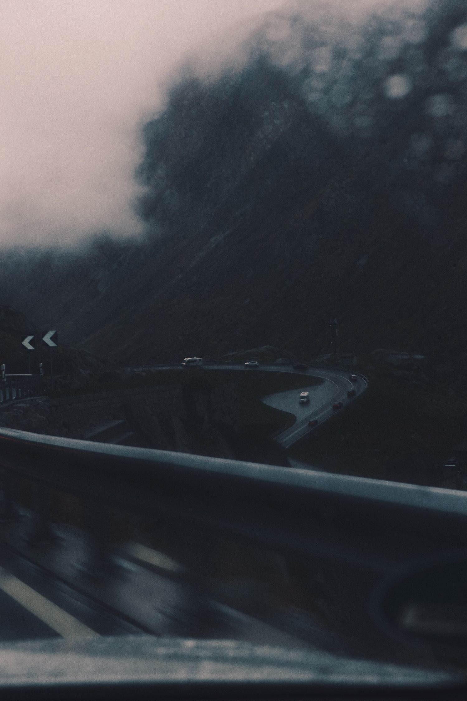 Rain-streaked windscreen view of a hairpin bend and chevron sign on the Gotthard Pass