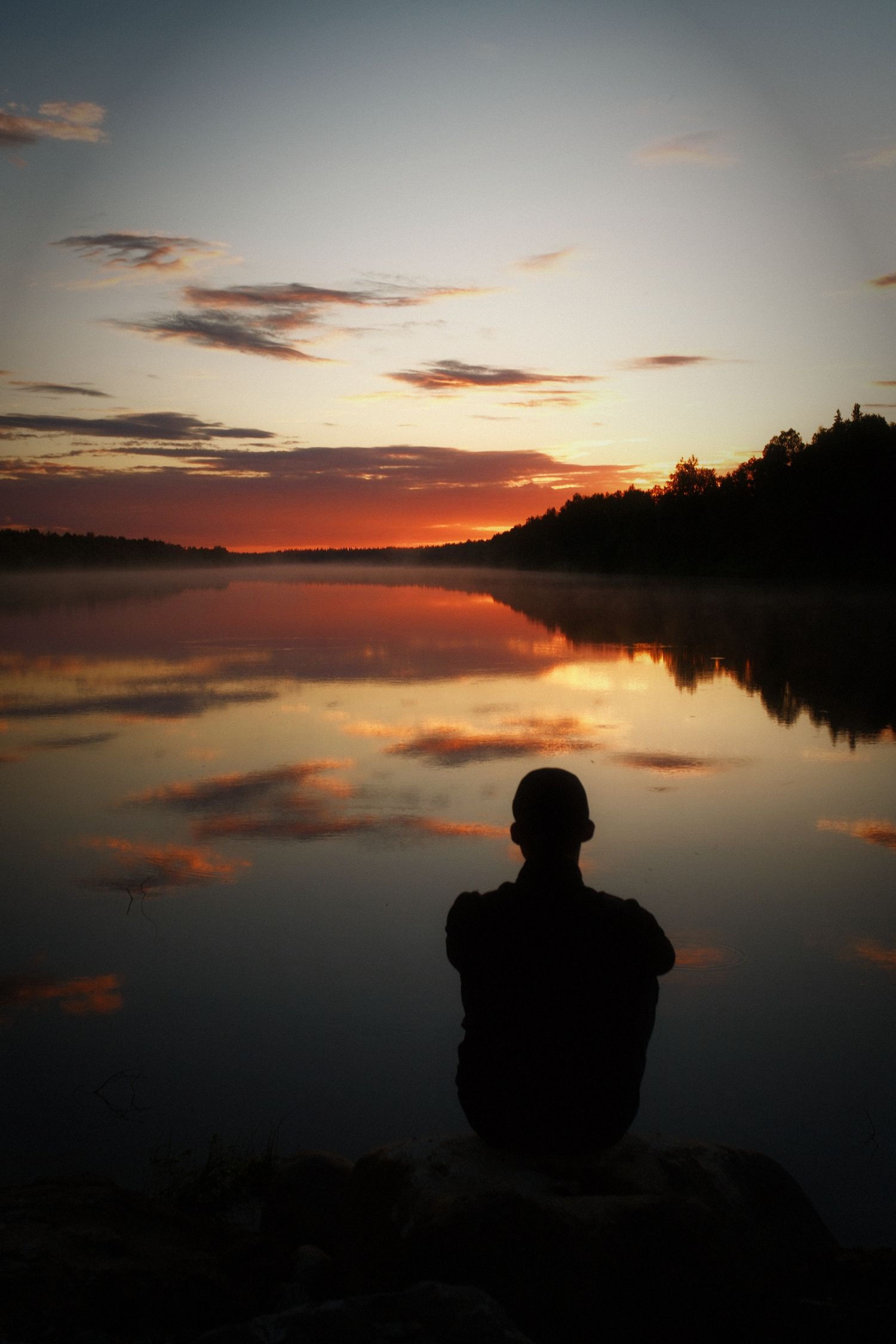 Silhouette of a man watching the sun go down over a glassy Scandinavian lake