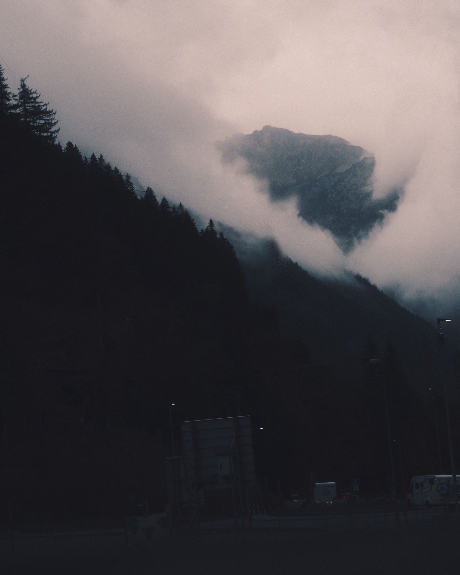 Rocky peak breaking through low cloud above dark pine forest on the Gotthard Pass