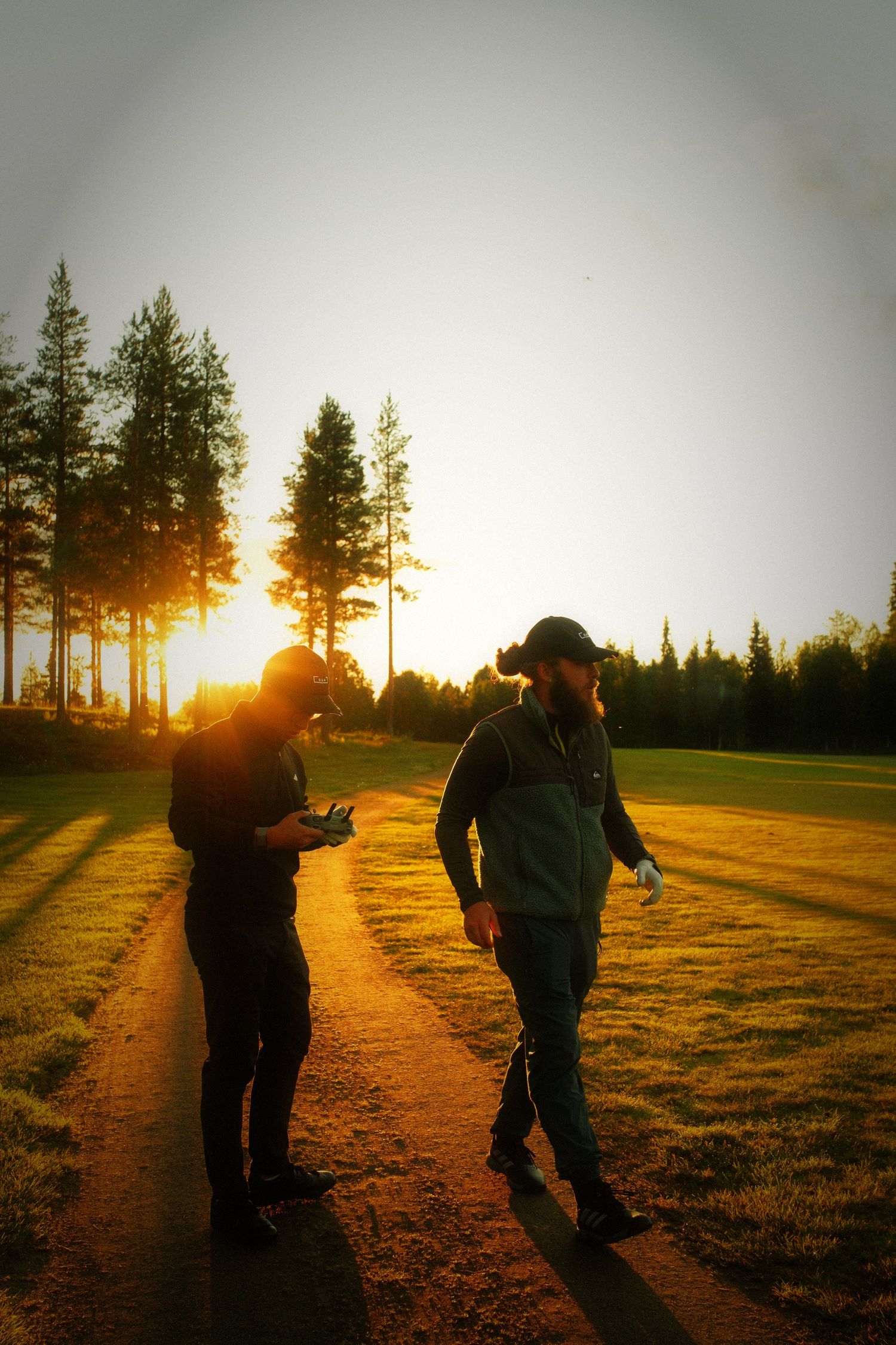 Two friends walking through a pine forest towards the low golden sun in Lapland