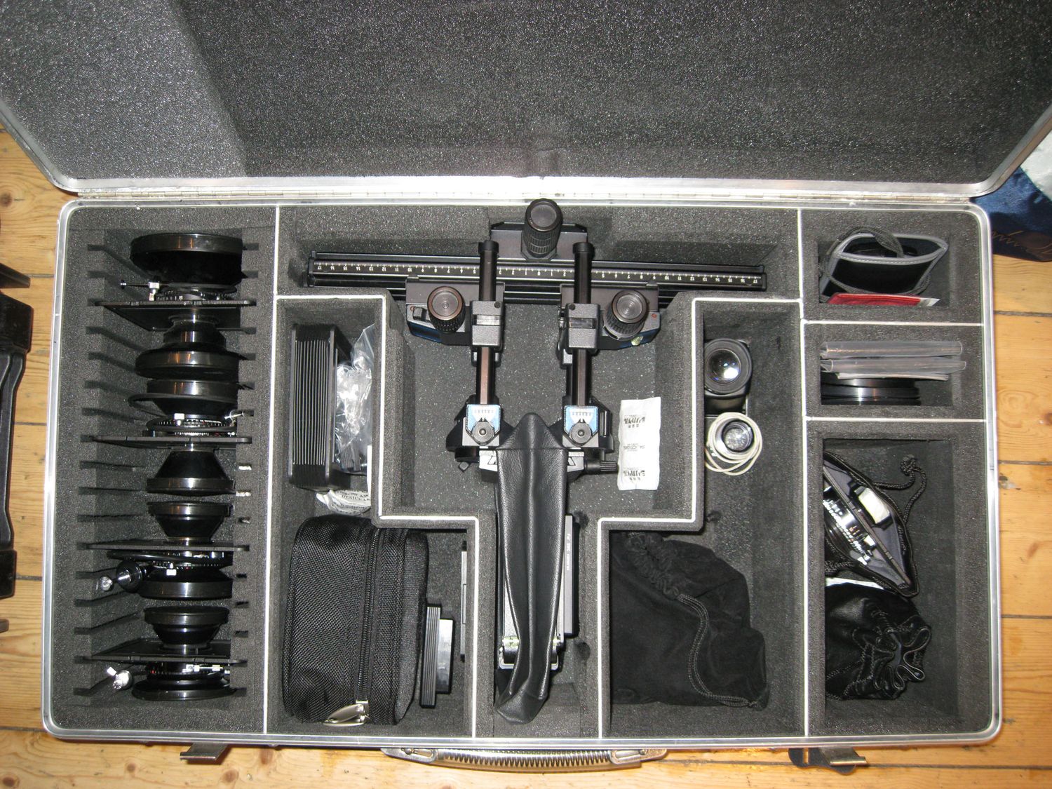 Professional camera equipment kit in foam-lined hard case with lenses, tripods, and accessories organized neatly.