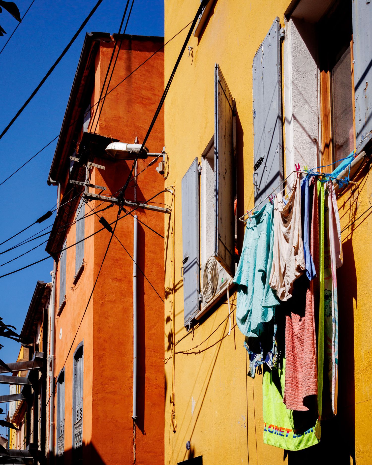 Colorful laundry hanging on a clothesline between vibrant orange and yellow buildings under blue sky.