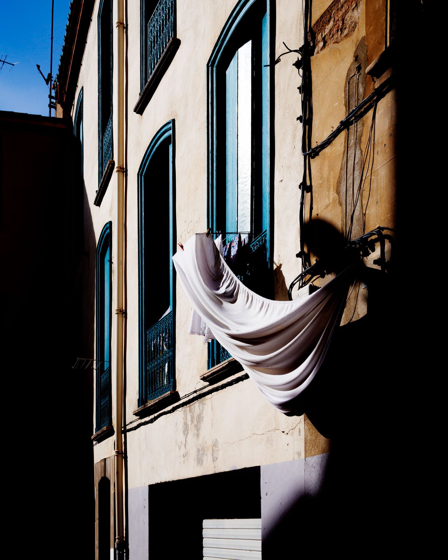 White laundry sheet billowing dramatically on a clothesline against an aged building facade in sunlight.