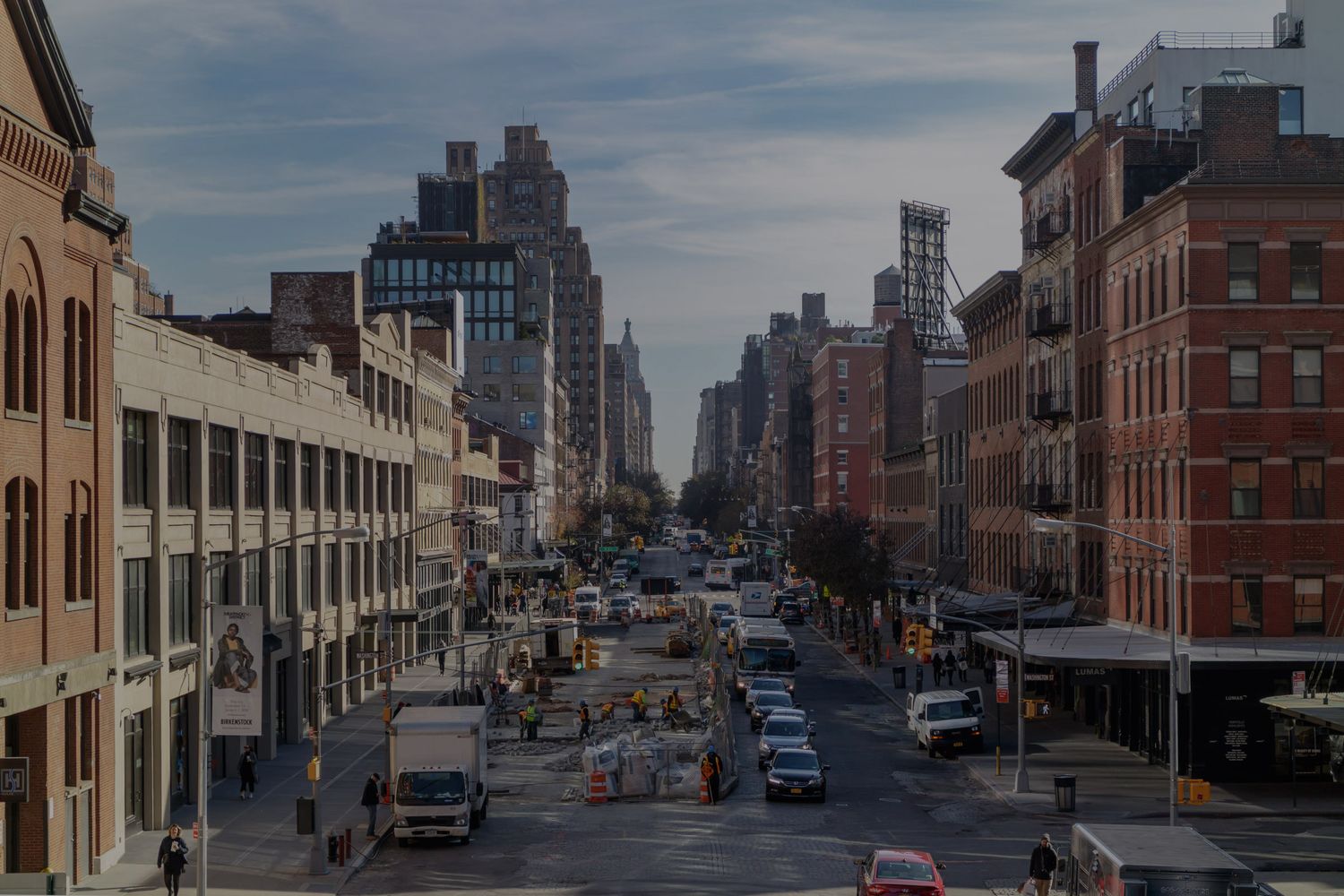 Busy urban street in New York City with brick buildings, traffic, and a city skyline stretching into the distance.