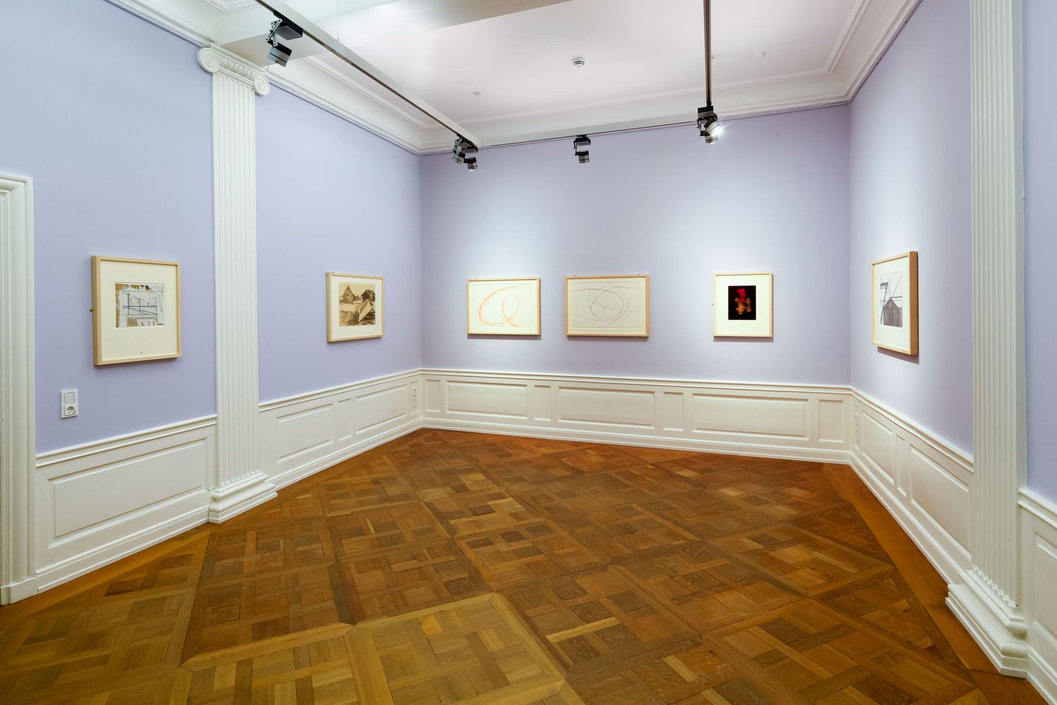 Art gallery with lavender walls displaying framed artwork on herringbone parquet floors under track lighting.