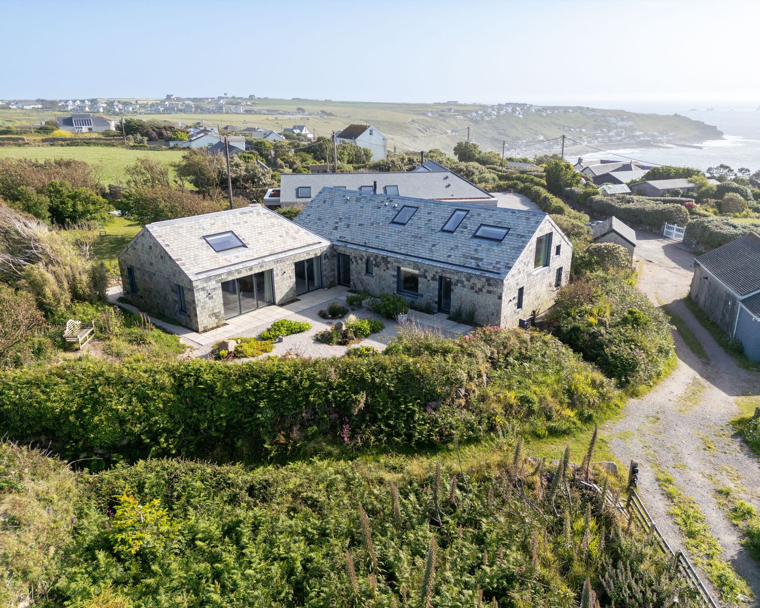 Aerial view of a stone coastal cottage surrounded by lush greenery with sweeping ocean bay views.